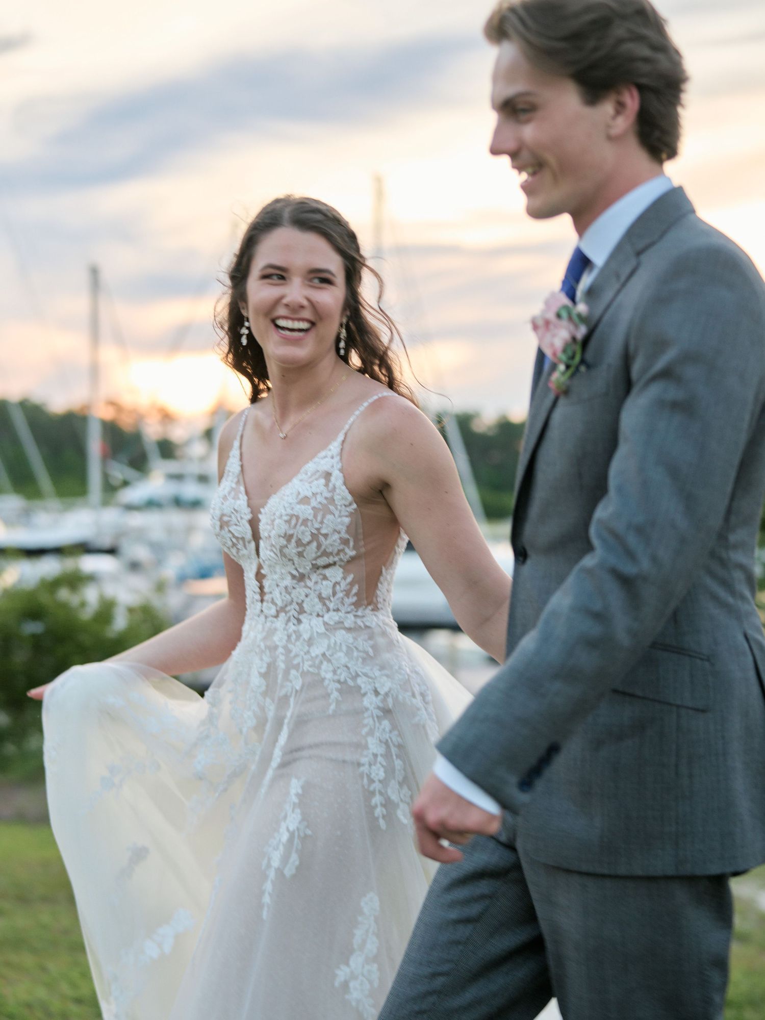 Couple shares a candid moment during their outdoor wedding at sunset by a marina.