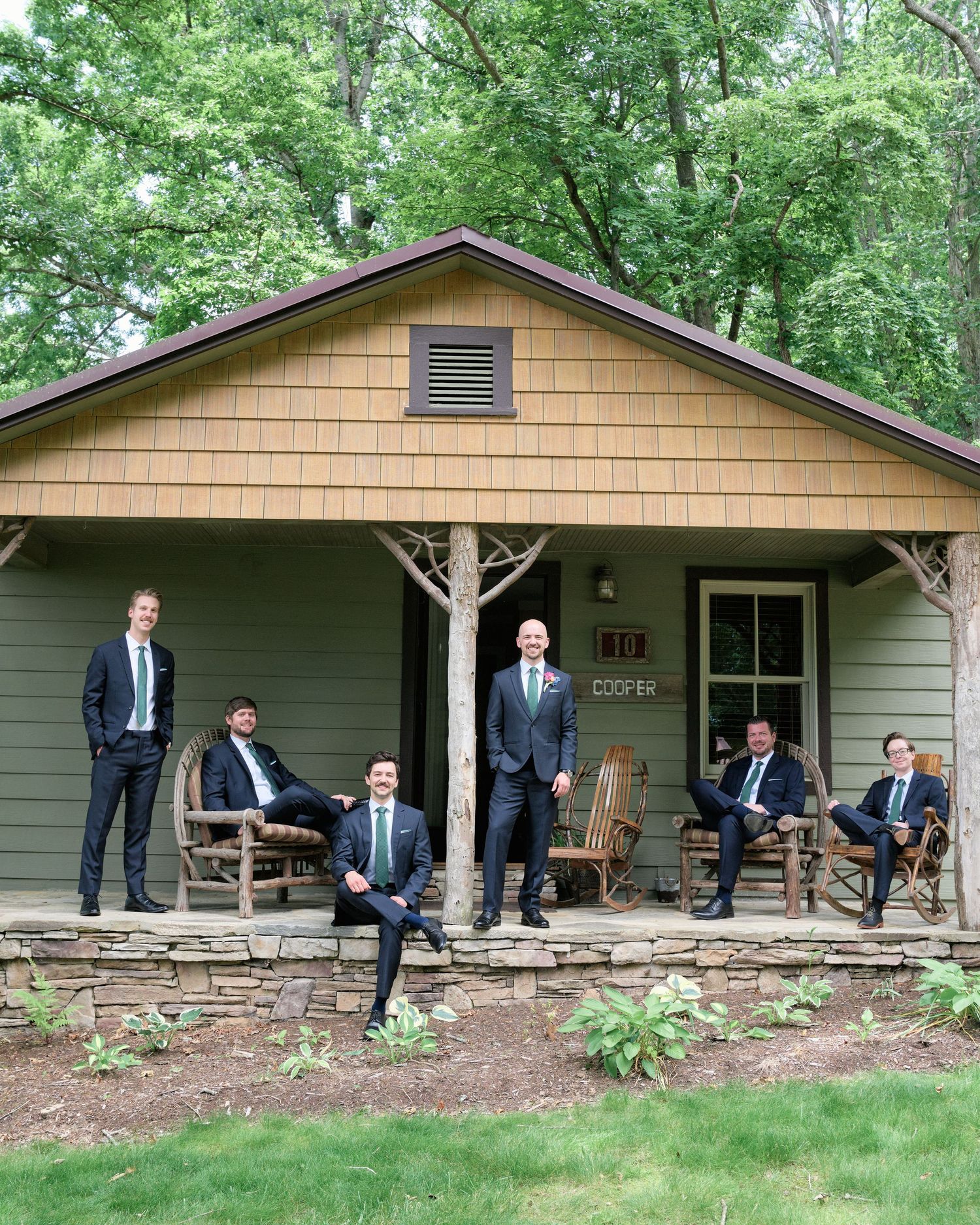 Groomsmen relaxing on rocking chairs on the porch of a rustic cabin.