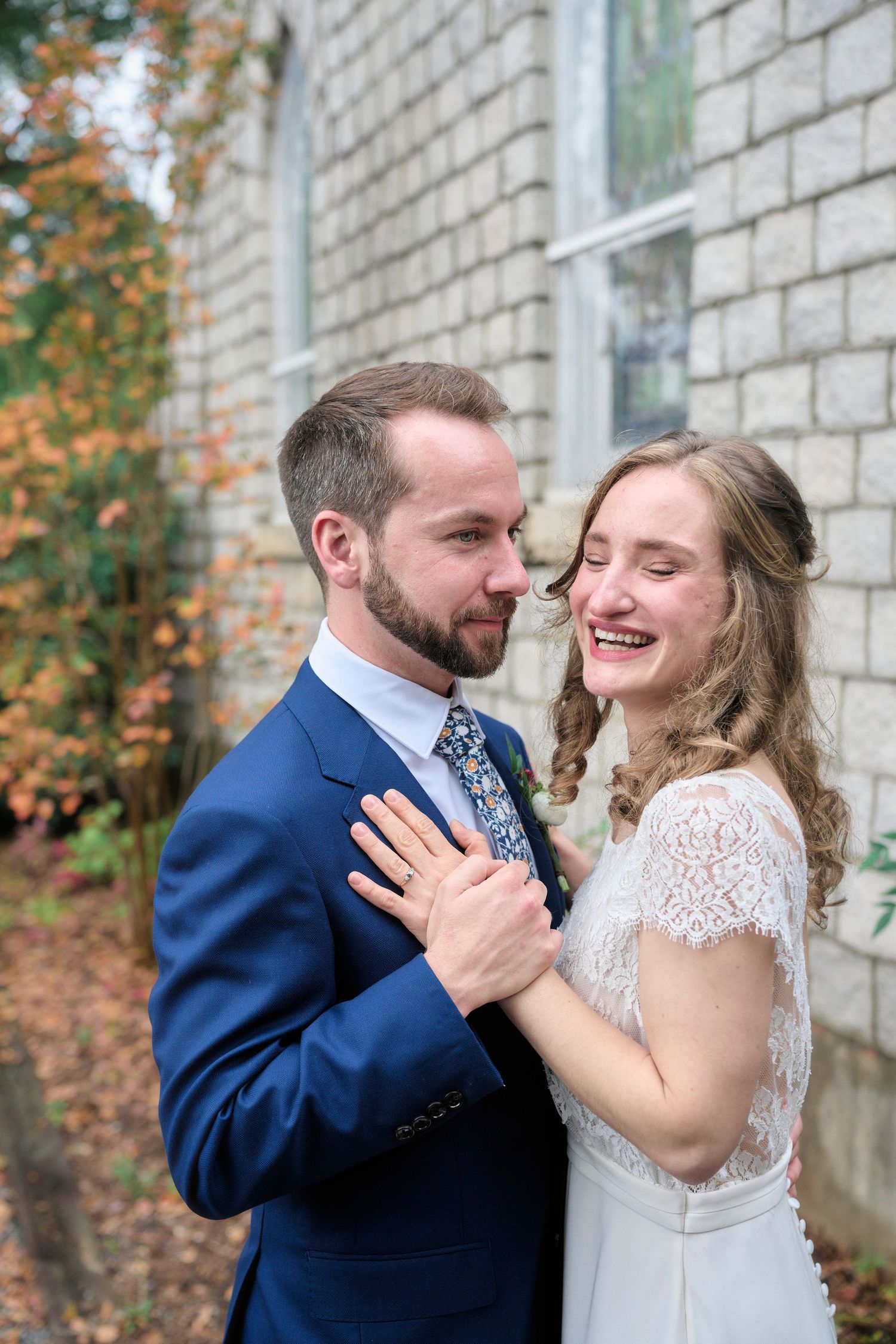 A joyful wedding portrait showing tender interaction between the bride and groom by a stone church wall.