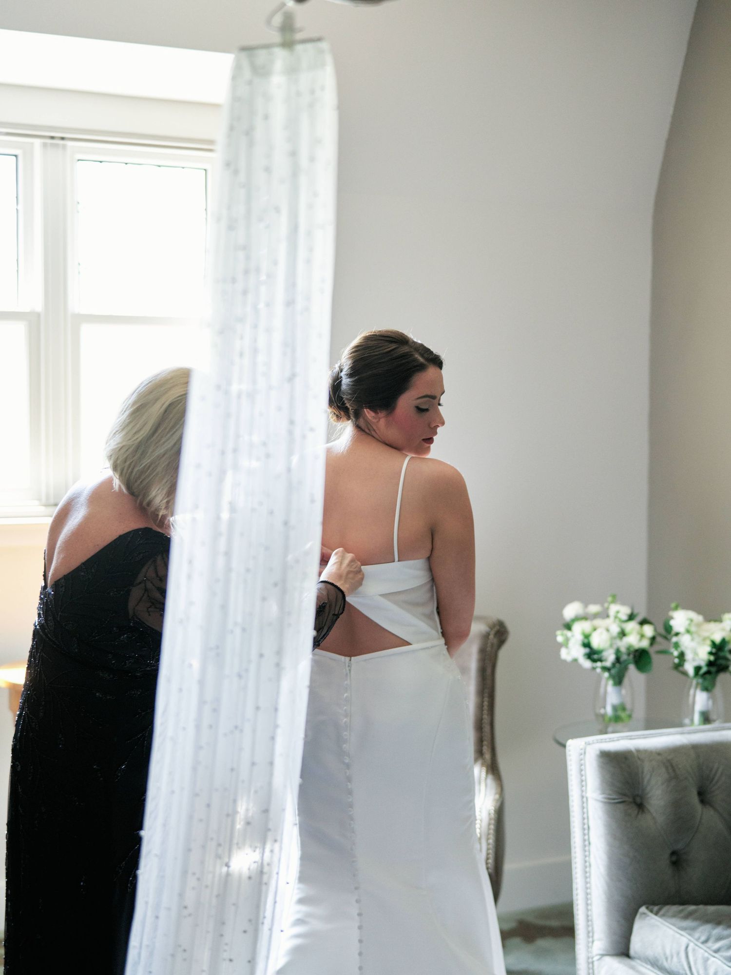 Mother helping her daughter the bride zip up her dress in a hotel room in Asheville.