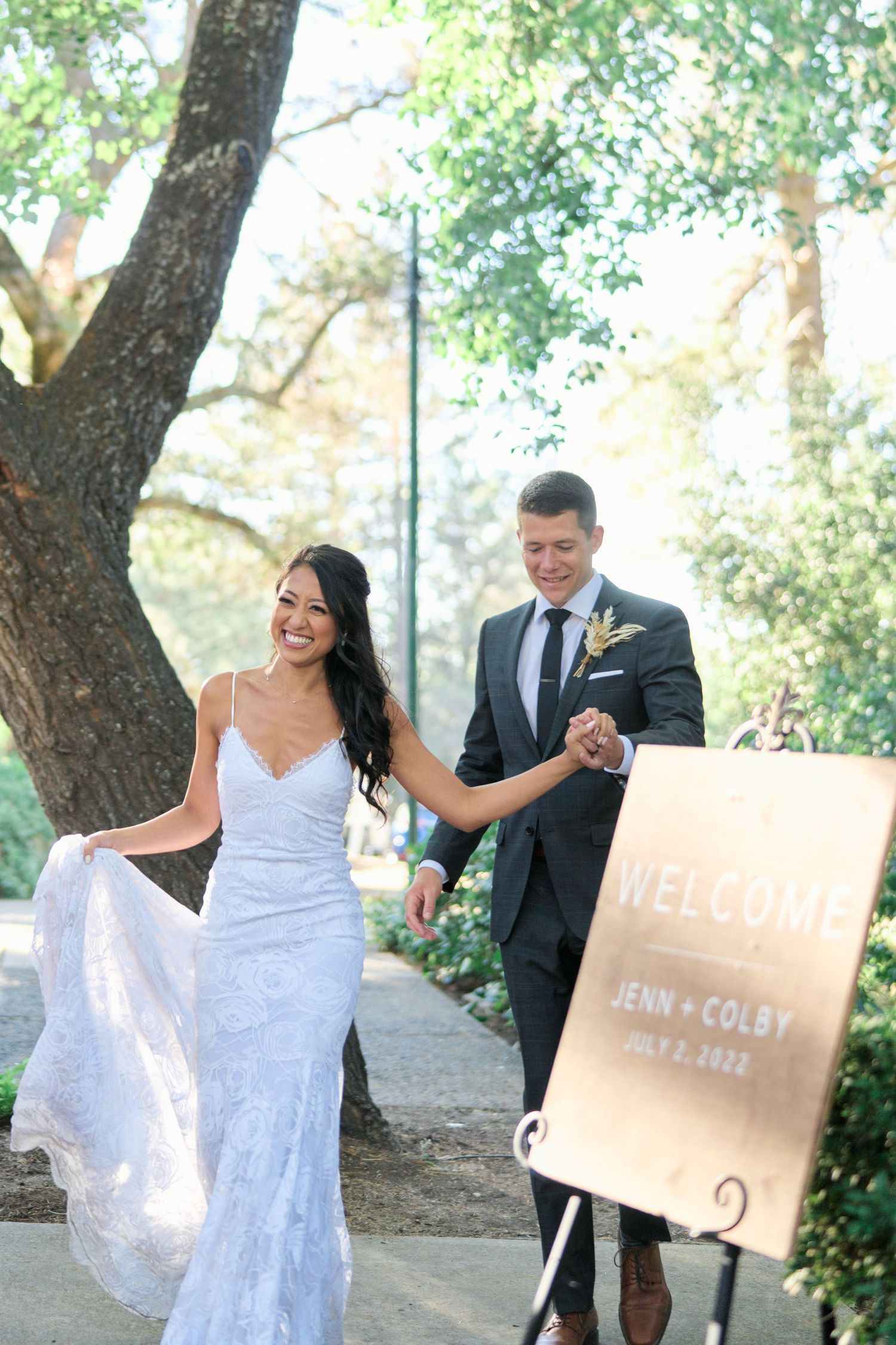 A couple walking along a garden path with a welcome sign for their wedding celebration.