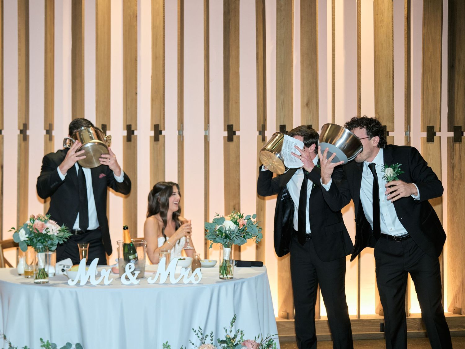 Groomsmen drinking from gold champagne buckets at a wedding reception with Mr & Mrs sign on the sweetheart table.