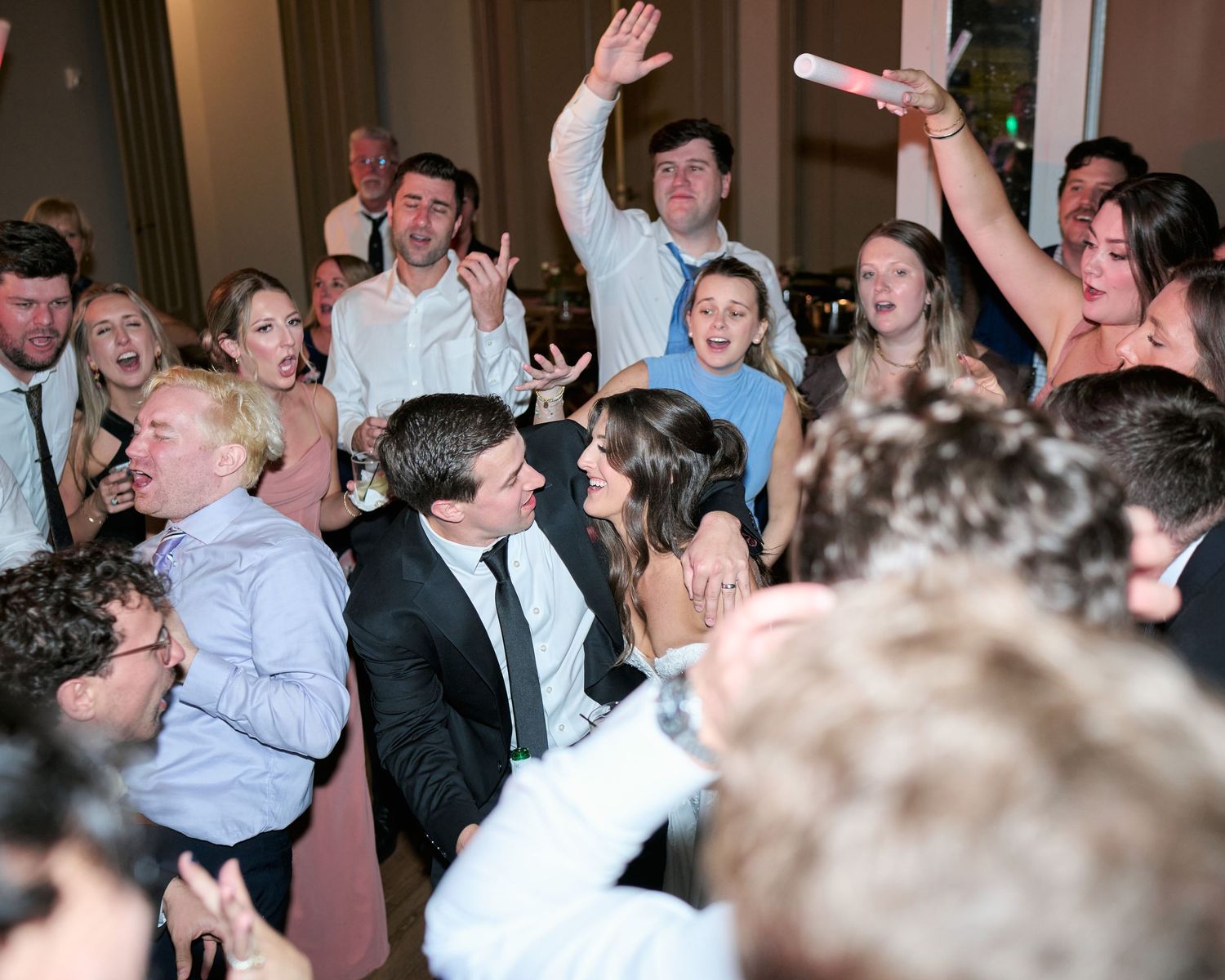 Joyful wedding reception guests dancing and celebrating on the dance floor at an elegant indoor venue.