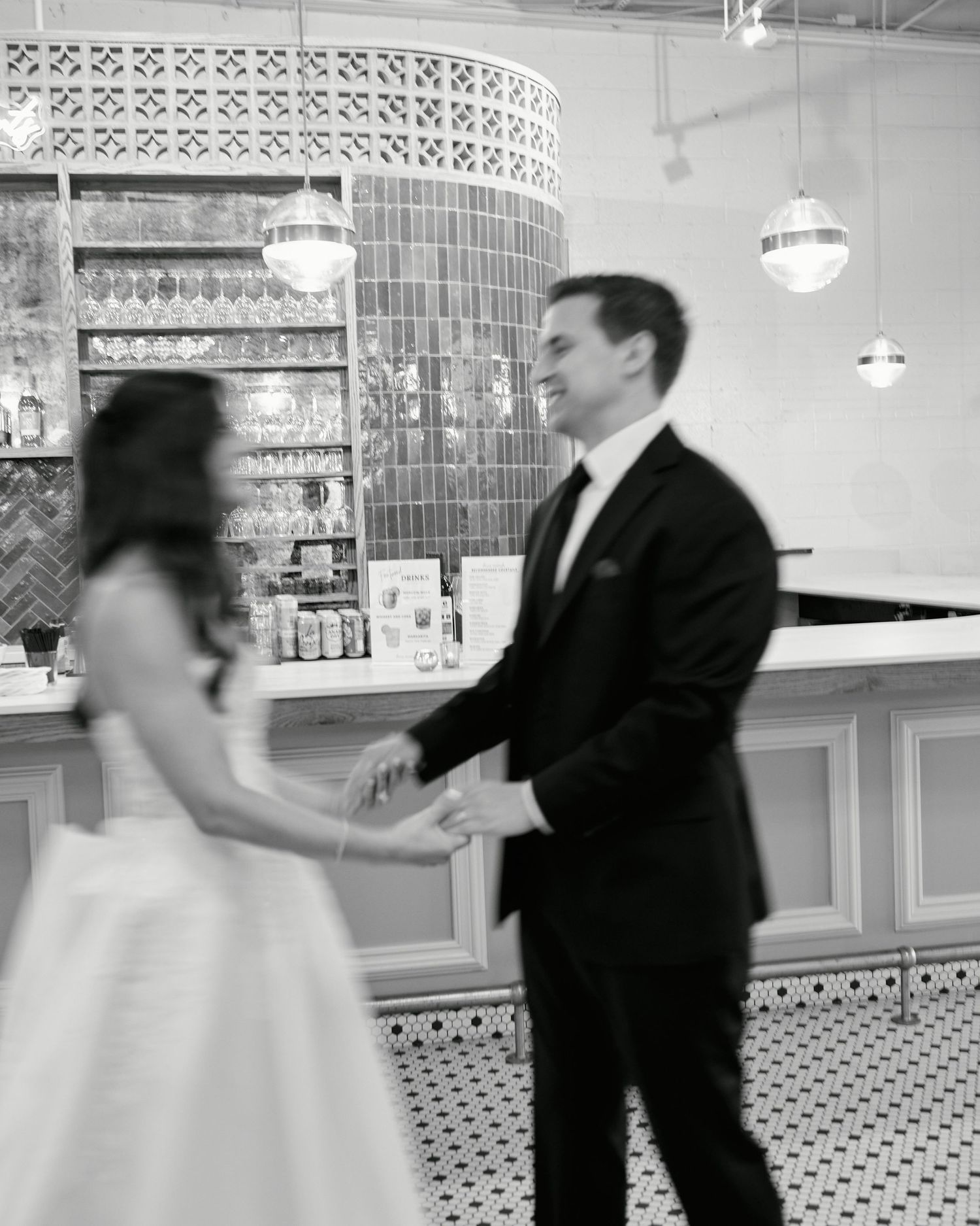 Black and white photo of a bride and groom dancing together in an elegant venue with pendant lights.