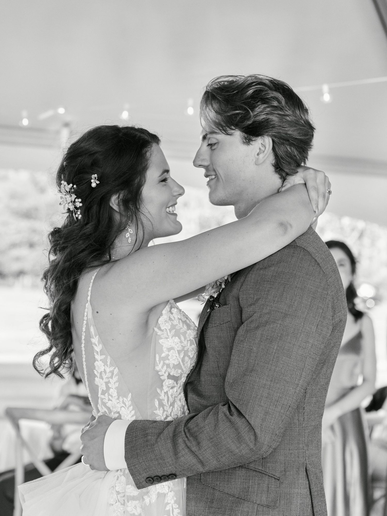 A romantic black and white wedding photo showing a loving couple dancing together under a tent with delicate floral details.