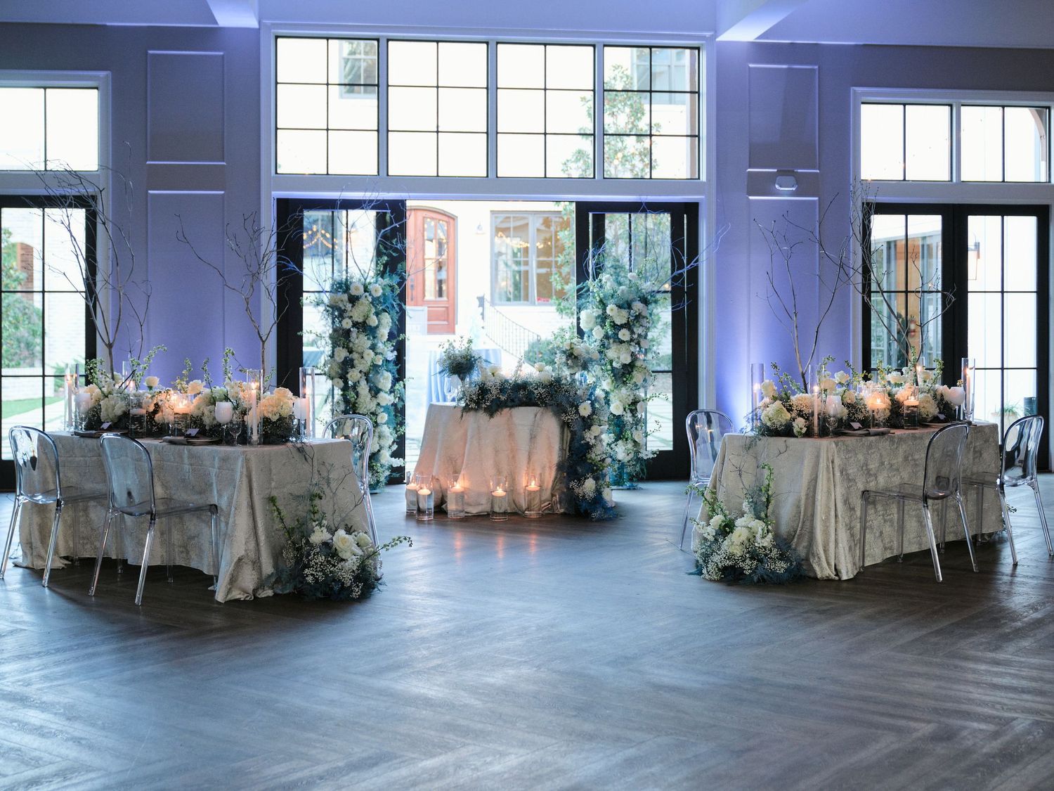 Elegant wedding reception venue with three decorated round tables and blue uplighting in a modern space.