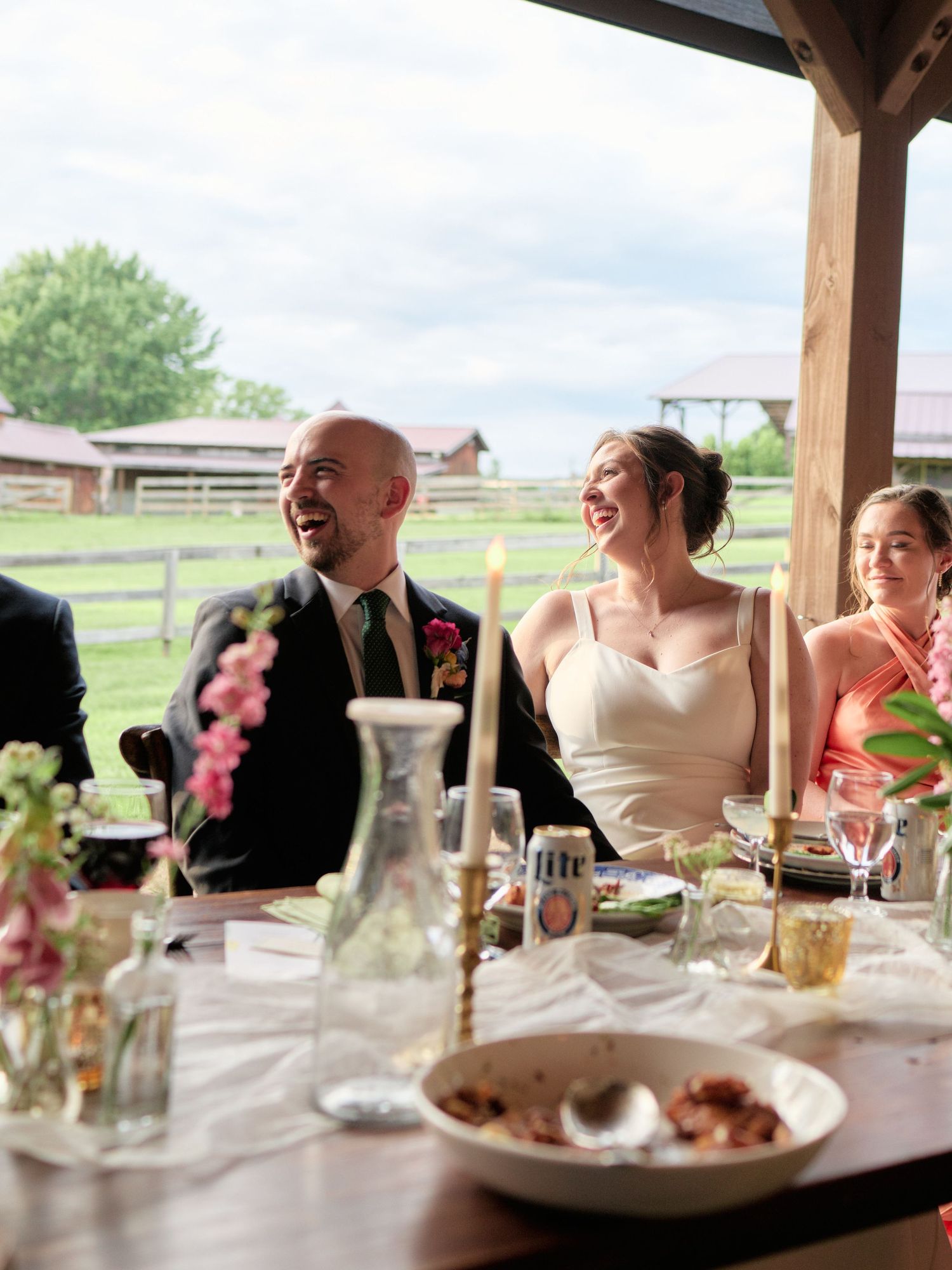 Wedding reception celebration at a rustic venue with elegant table settings overlooking farm fields and fencing.