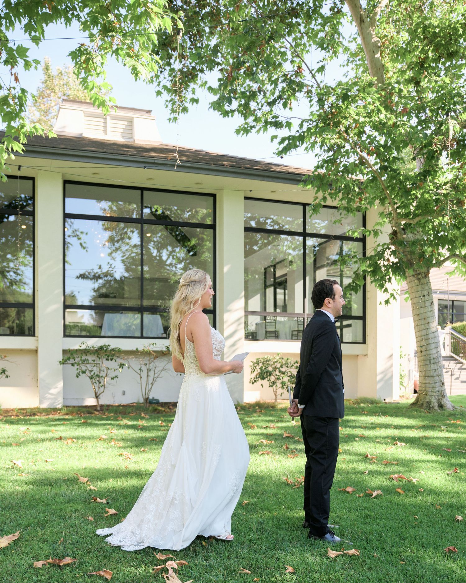 A first look wedding moment captured outside a modern building with large windows.