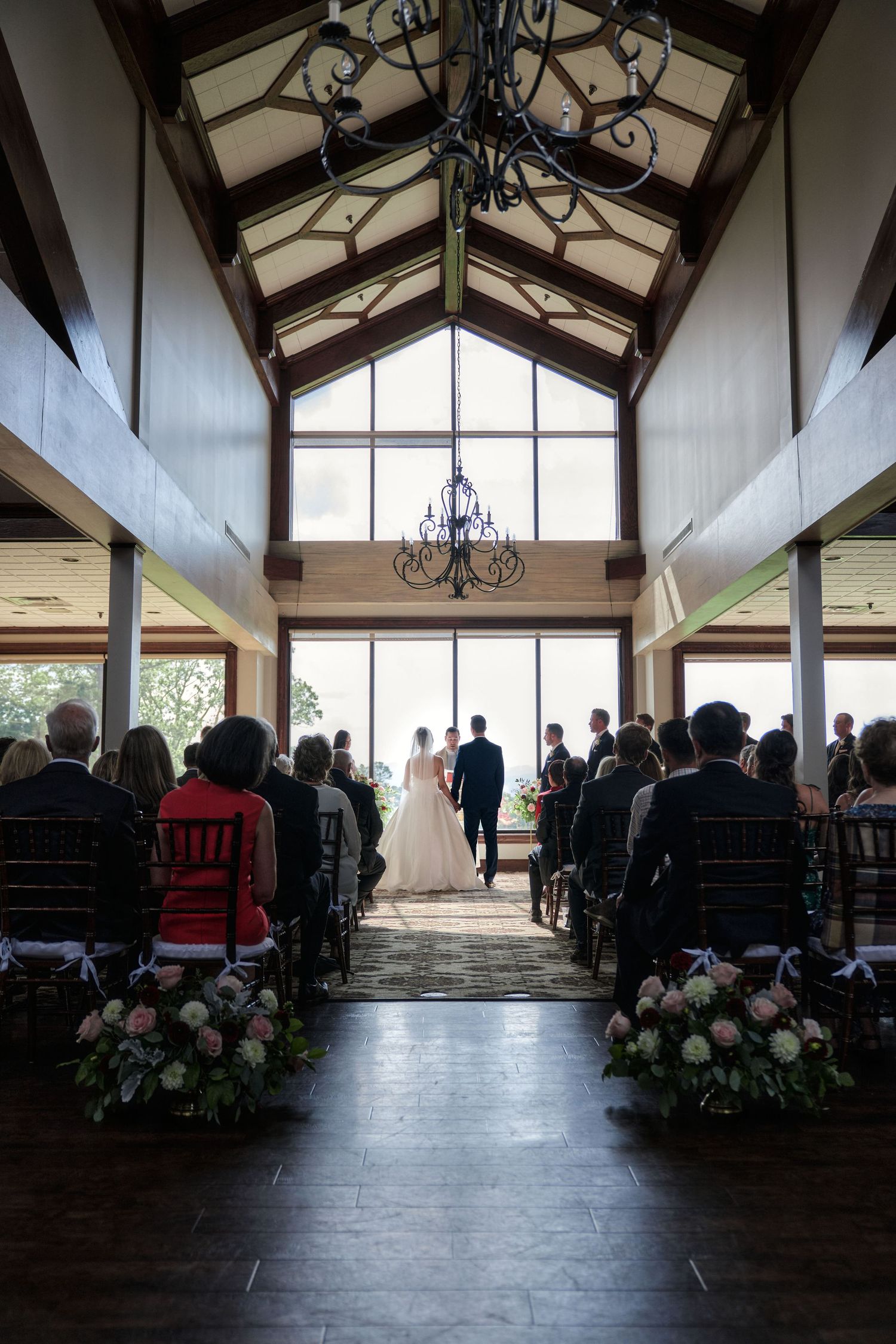 Indoor wedding ceremony with exposed beam ceiling and wrought iron chandelier in natural light.