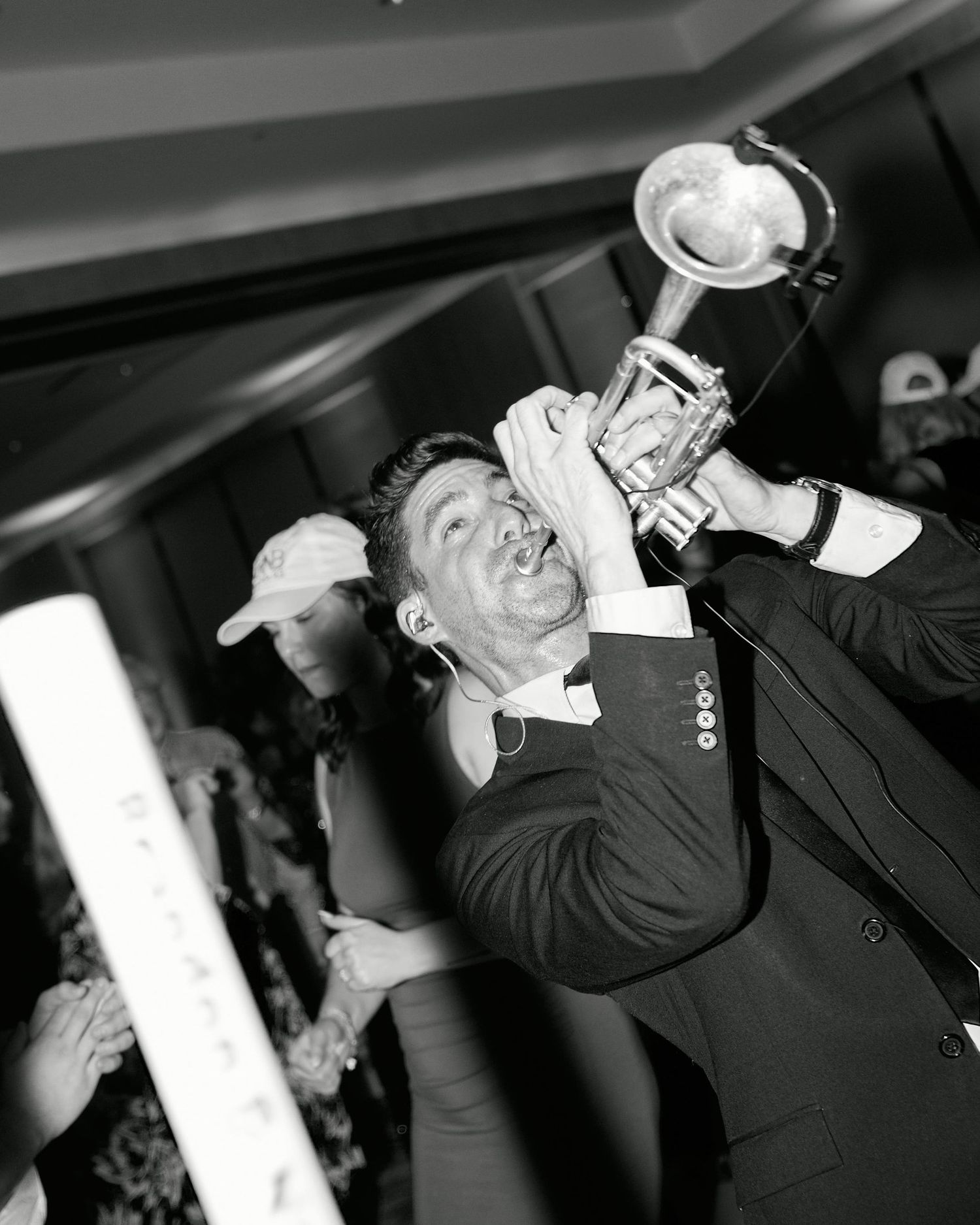 Black and white image showing a musician in a suit enthusiastically playing a trumpet under stage lighting.