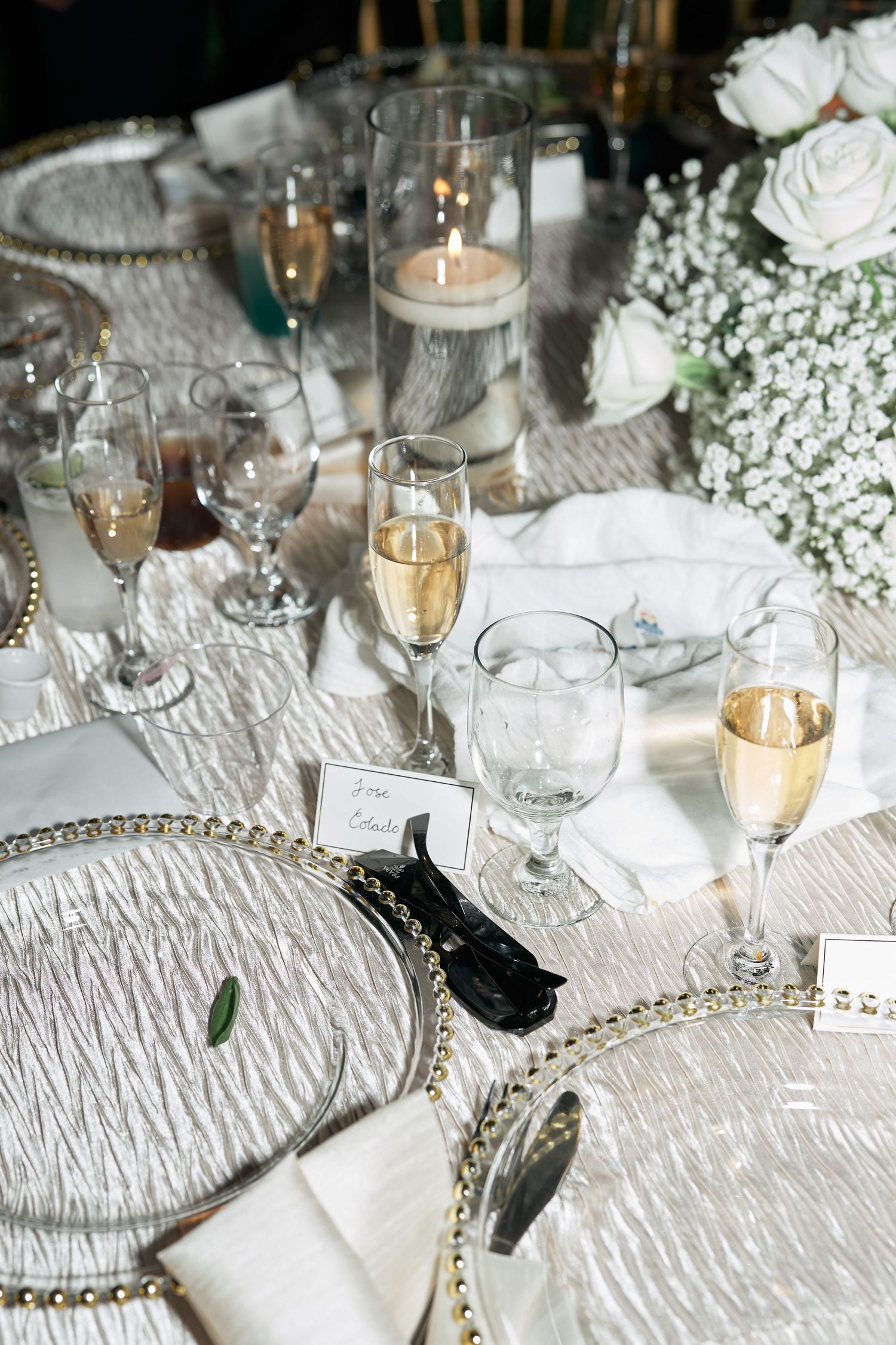 Elegant wedding reception table setting with champagne glasses, white roses, and crystal plates.