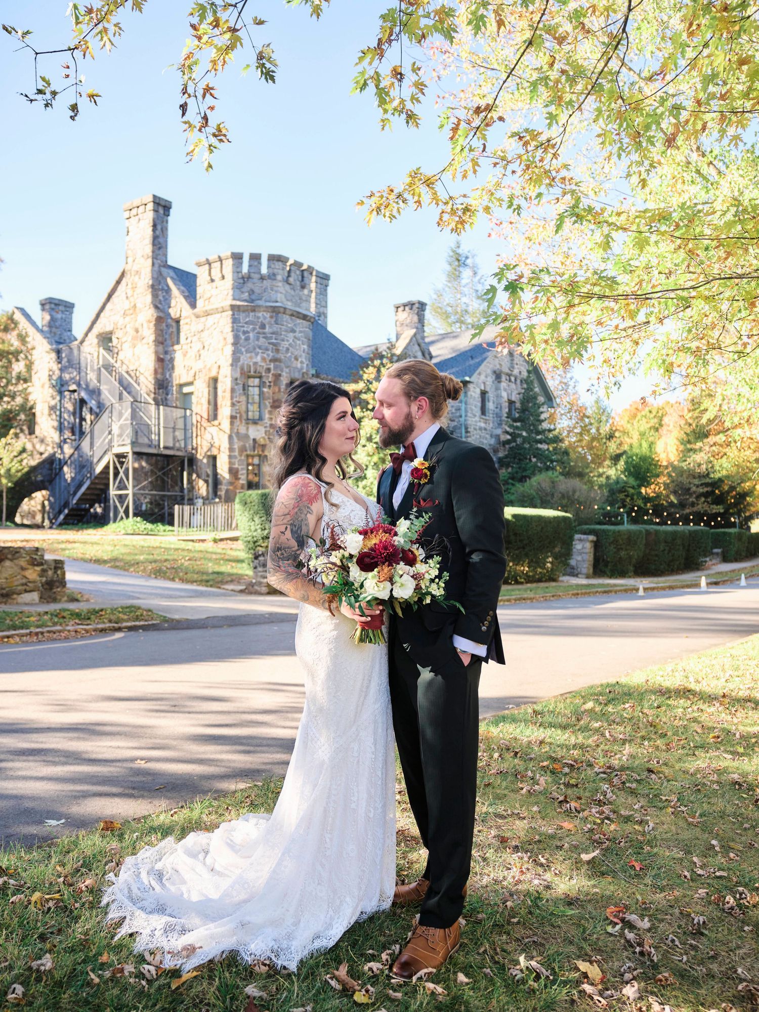 Couple poses with castle-like building in background during autumn wedding photoshoot.