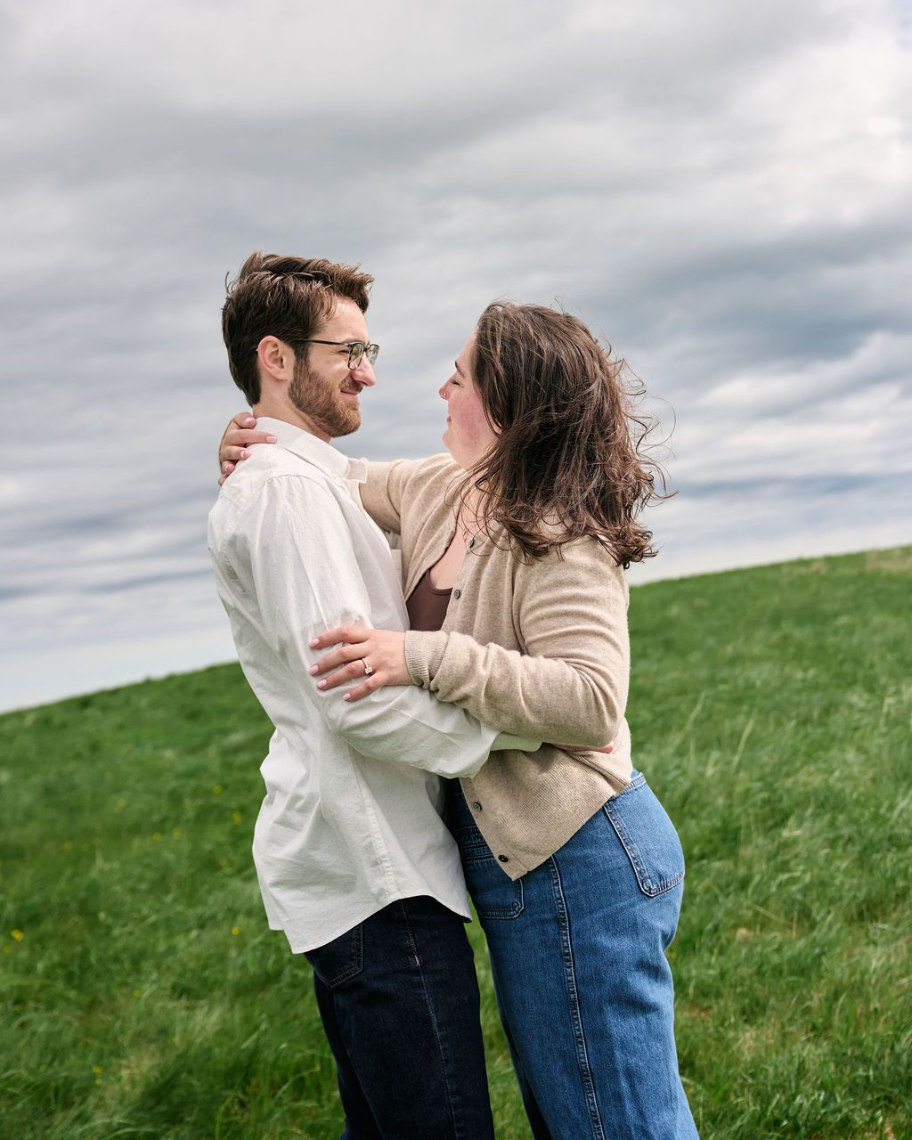 A couple embraces and spins together on a green hillside under cloudy skies.
