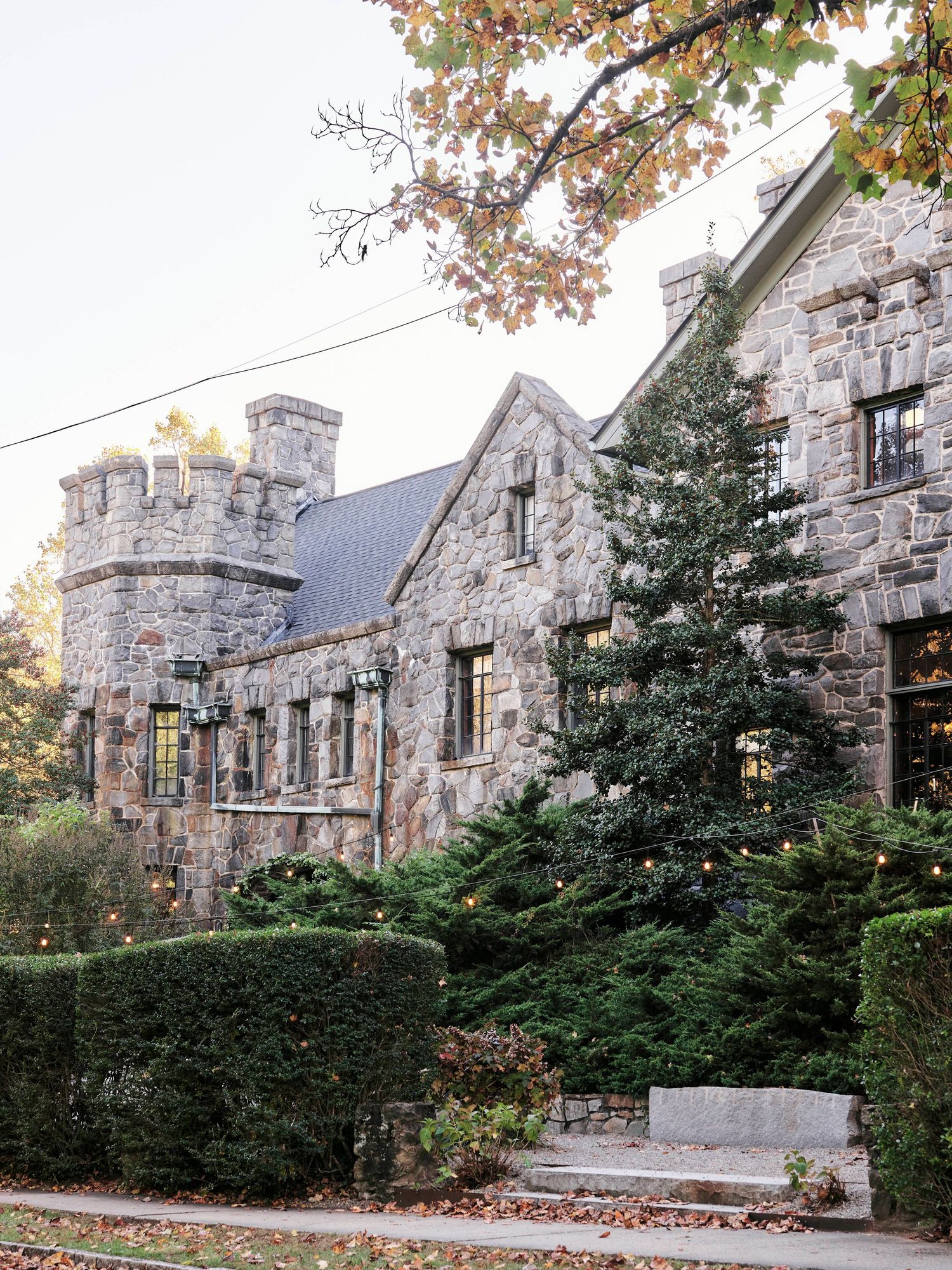A stone castle-style building with turrets surrounded by evergreen trees and autumn foliage.