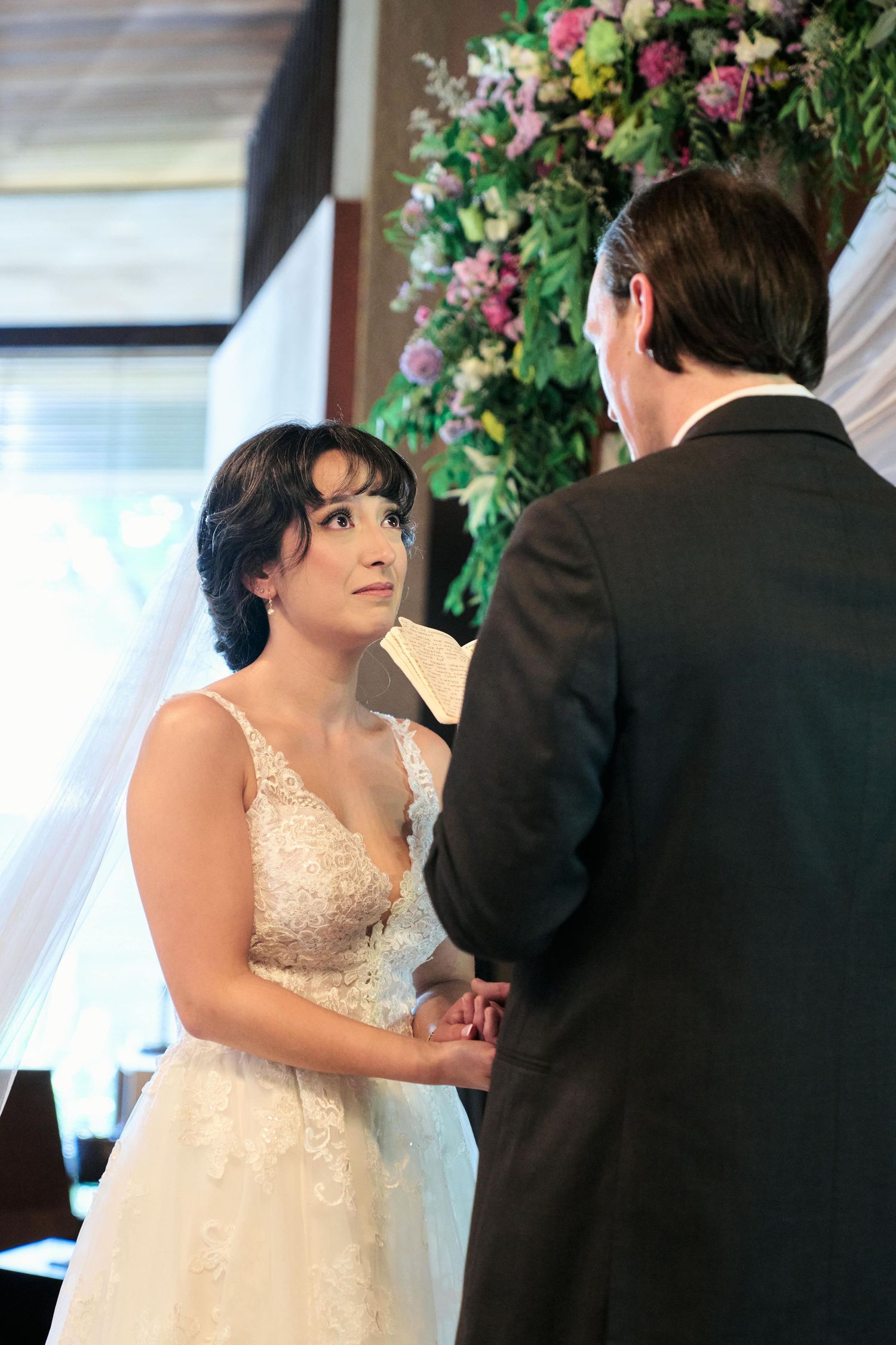 A couple sharing an intimate moment during their wedding ceremony under a floral arch.