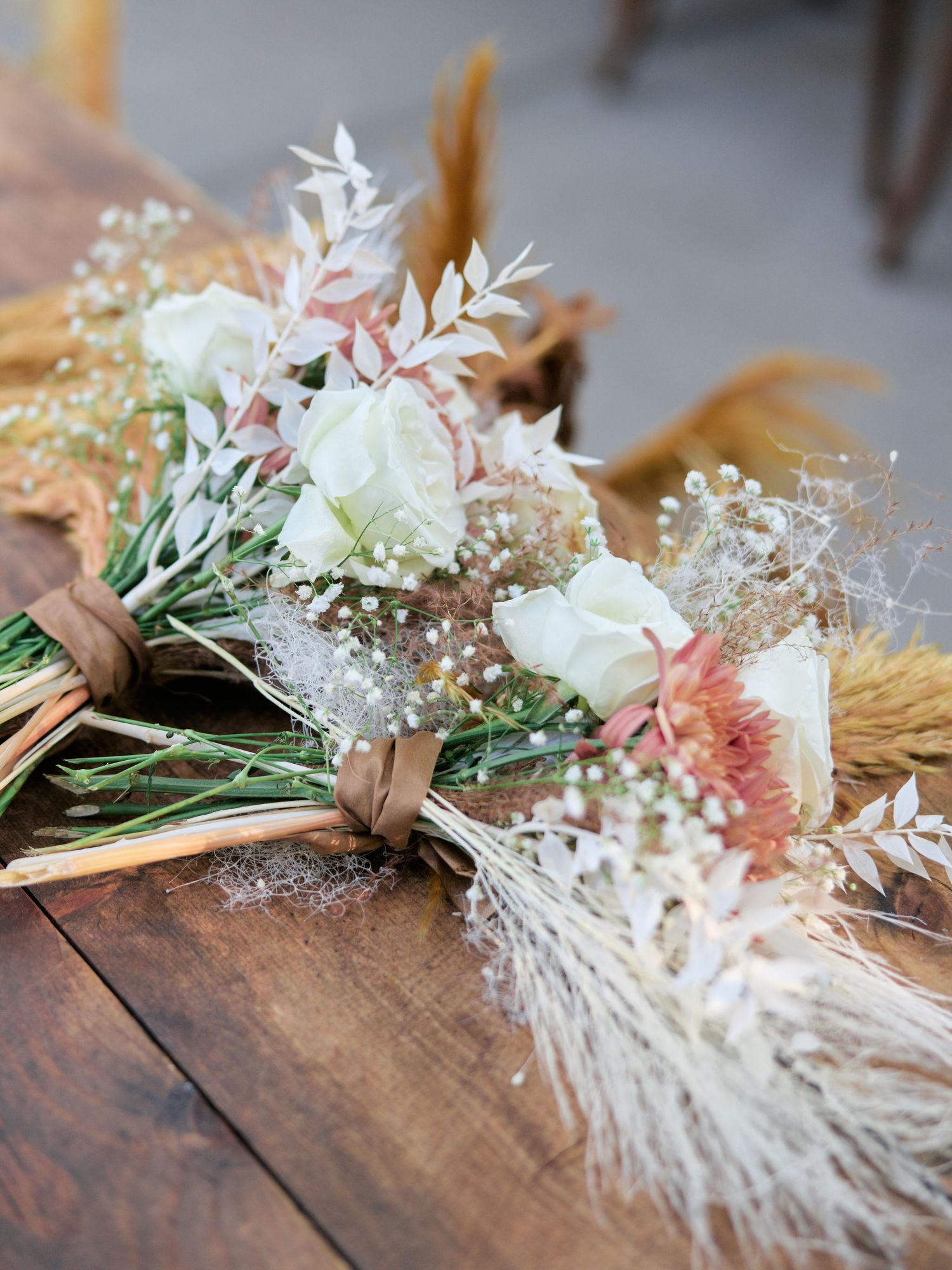 Romantic wedding bouquet with white roses, dried flowers, and pampas grass on wooden surface.