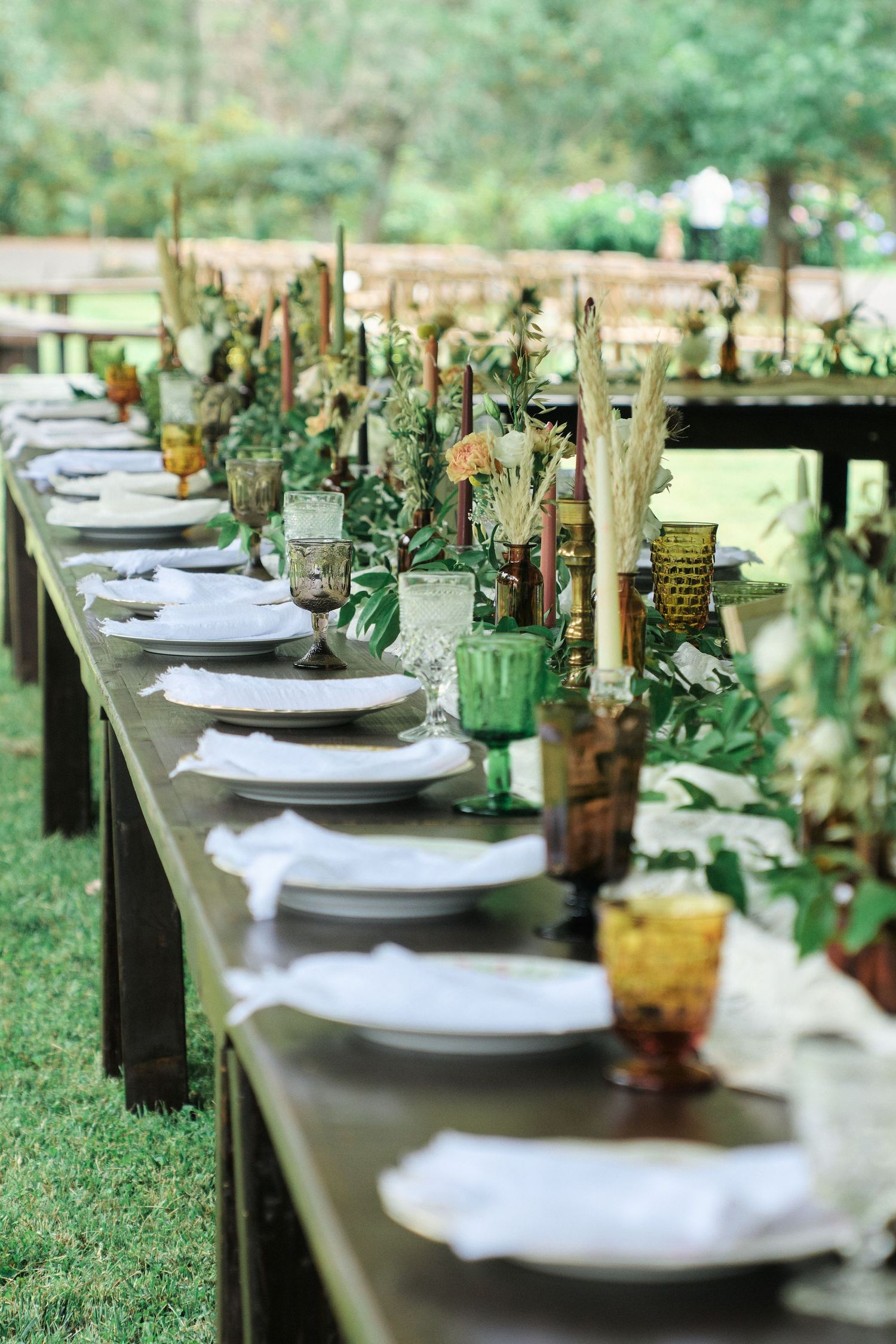 Elegant tablescape with vintage glassware, white plates and botanical centerpieces for outdoor reception.
