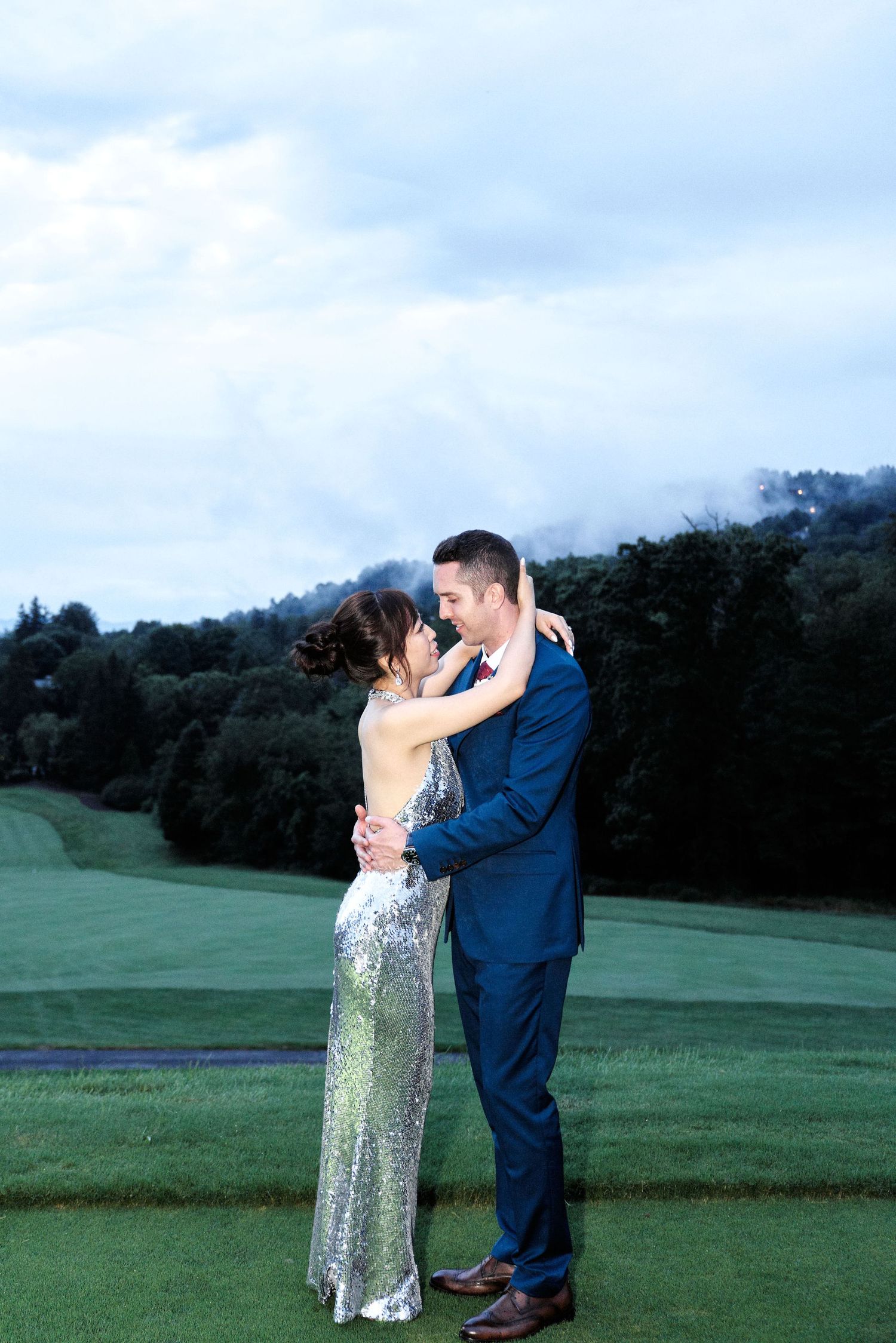 A couple shares a romantic embrace on a lush green golf course at twilight.