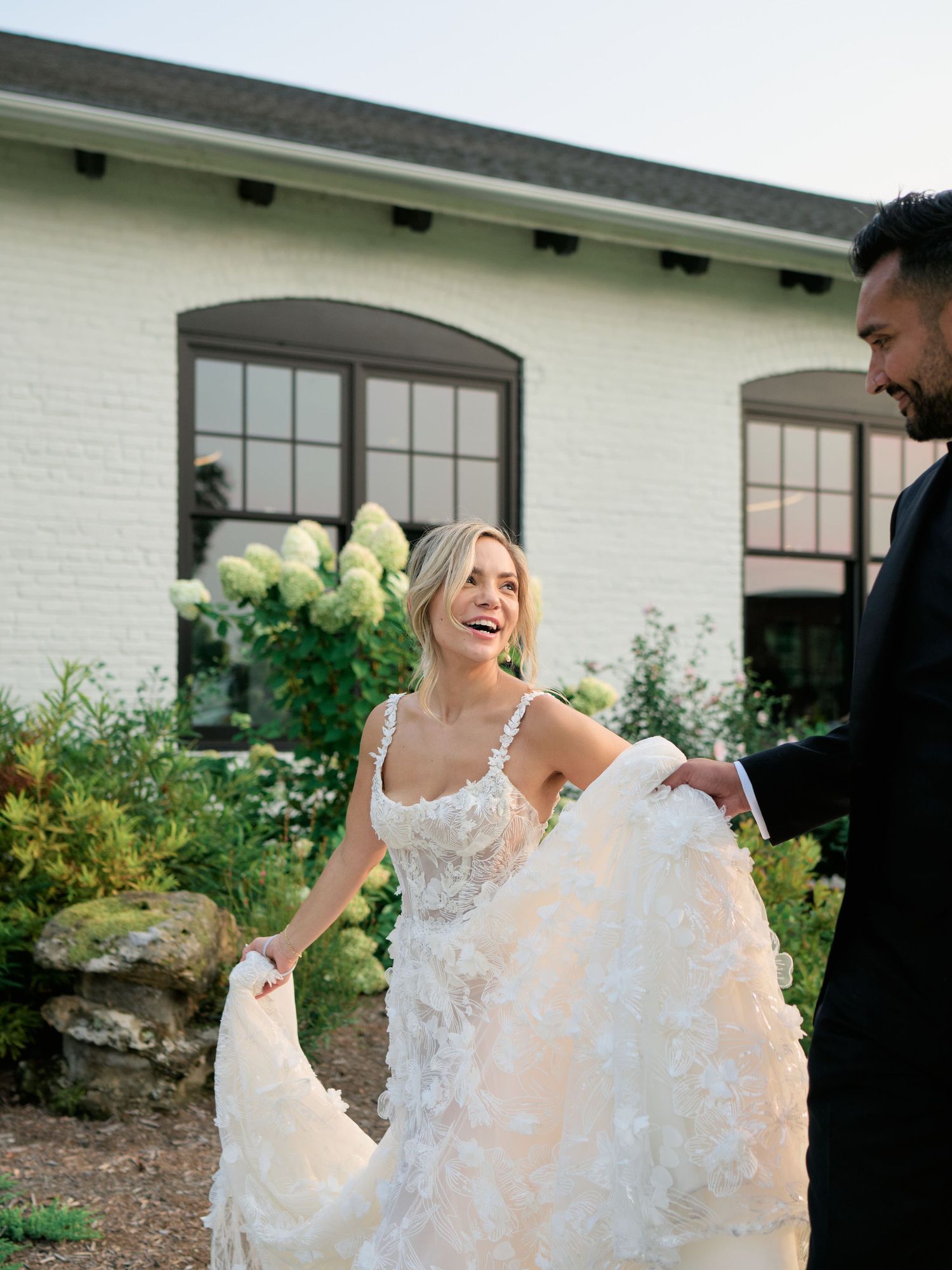 Joyful couple sharing a candid moment outdoors near a white building with lush garden and windows.