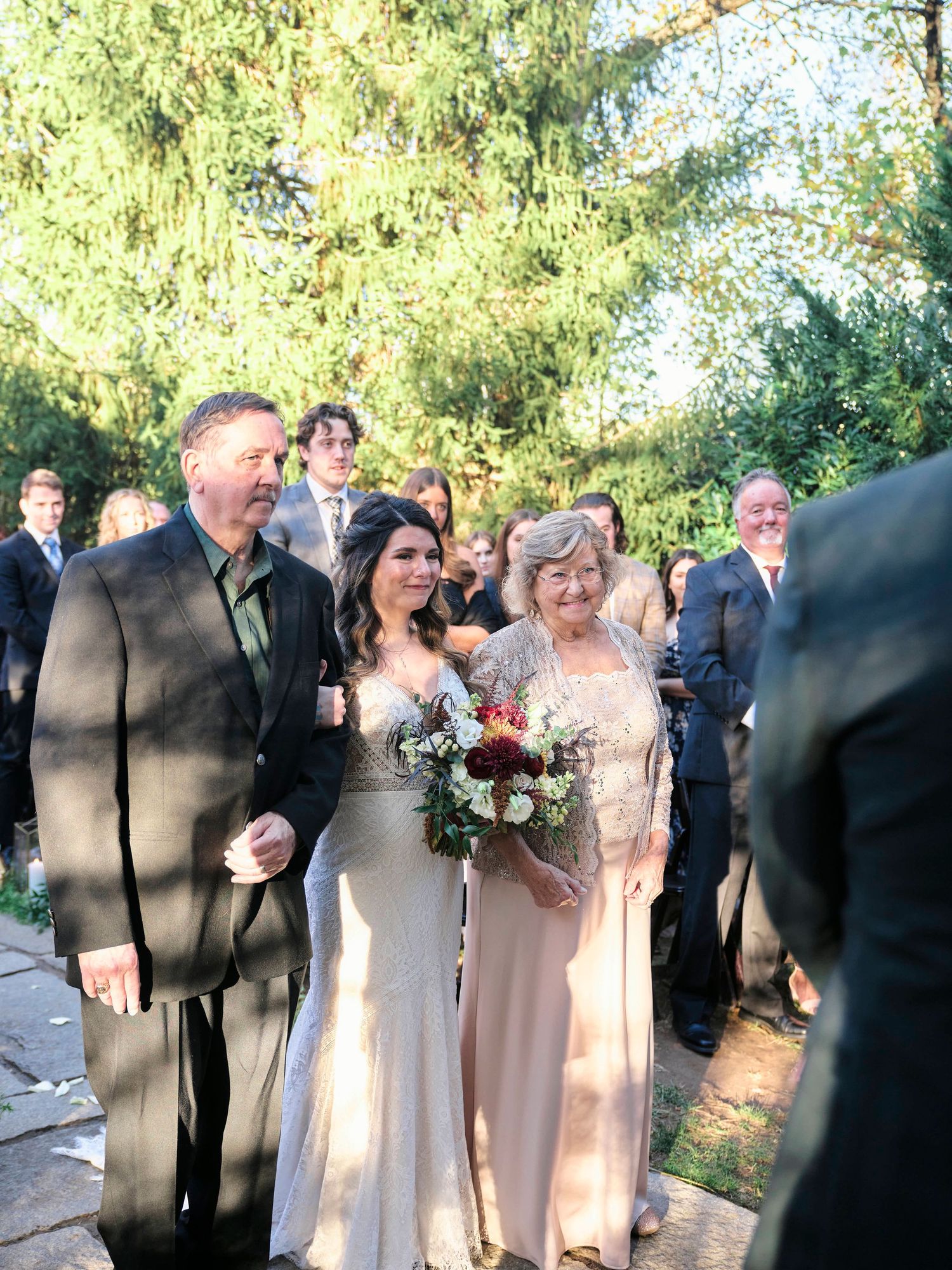 Wedding party gathered outdoors under tall evergreen trees during autumn ceremony.