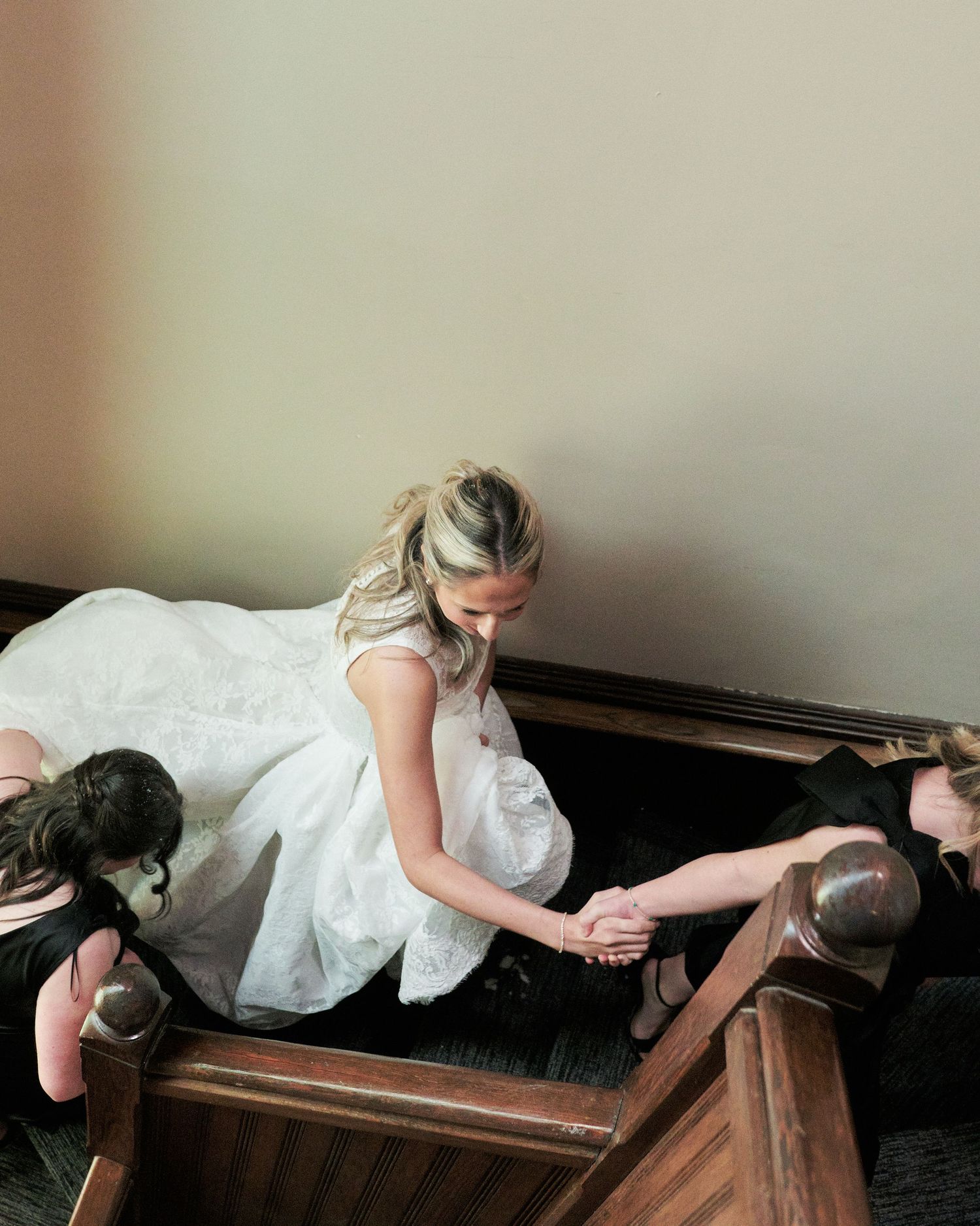 Bride in white gown holds hands with guests in church pew, viewed from above during wedding ceremony.