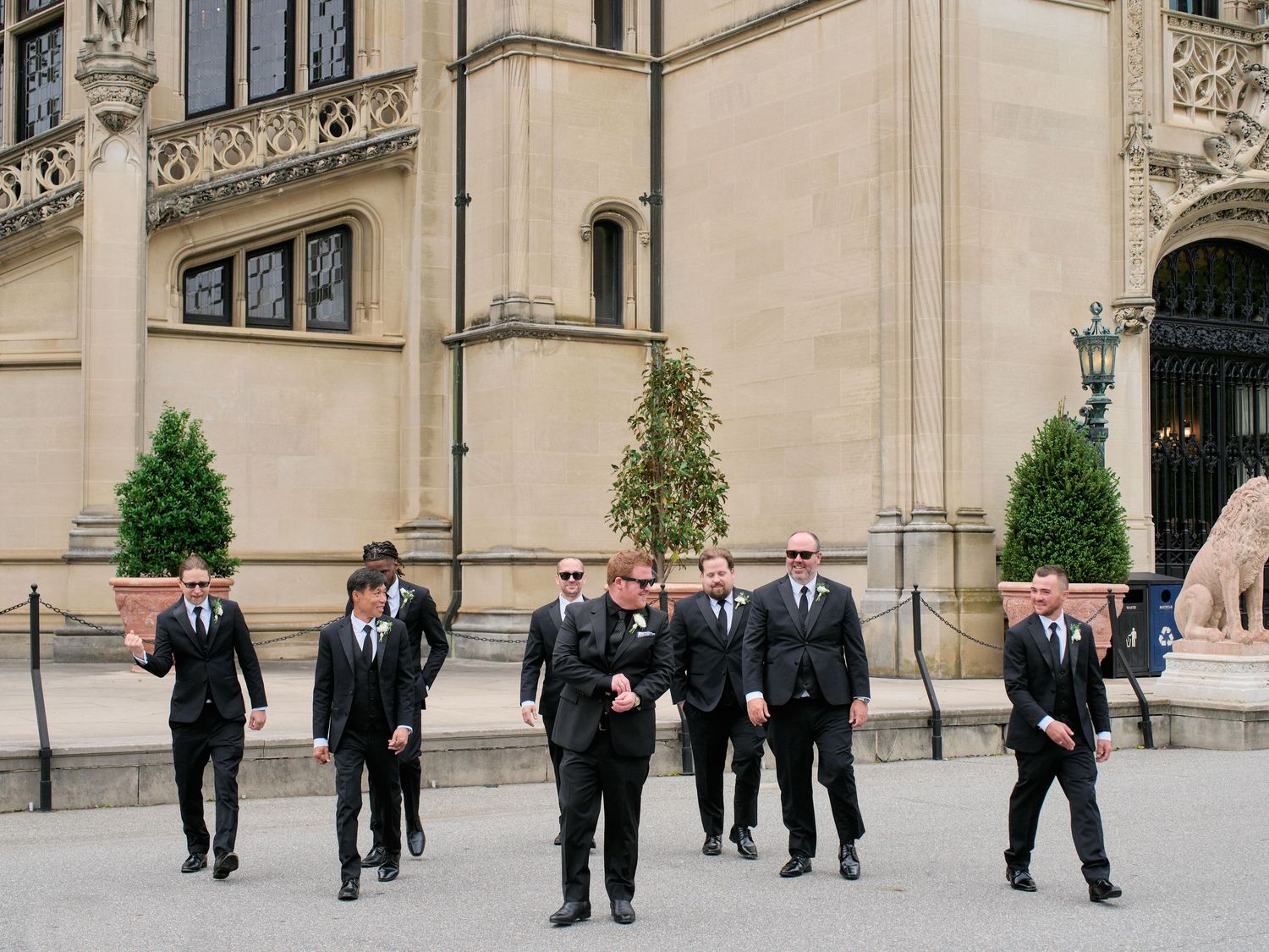 Group of formally dressed people walking and conversing in front of an ornate stone building facade.