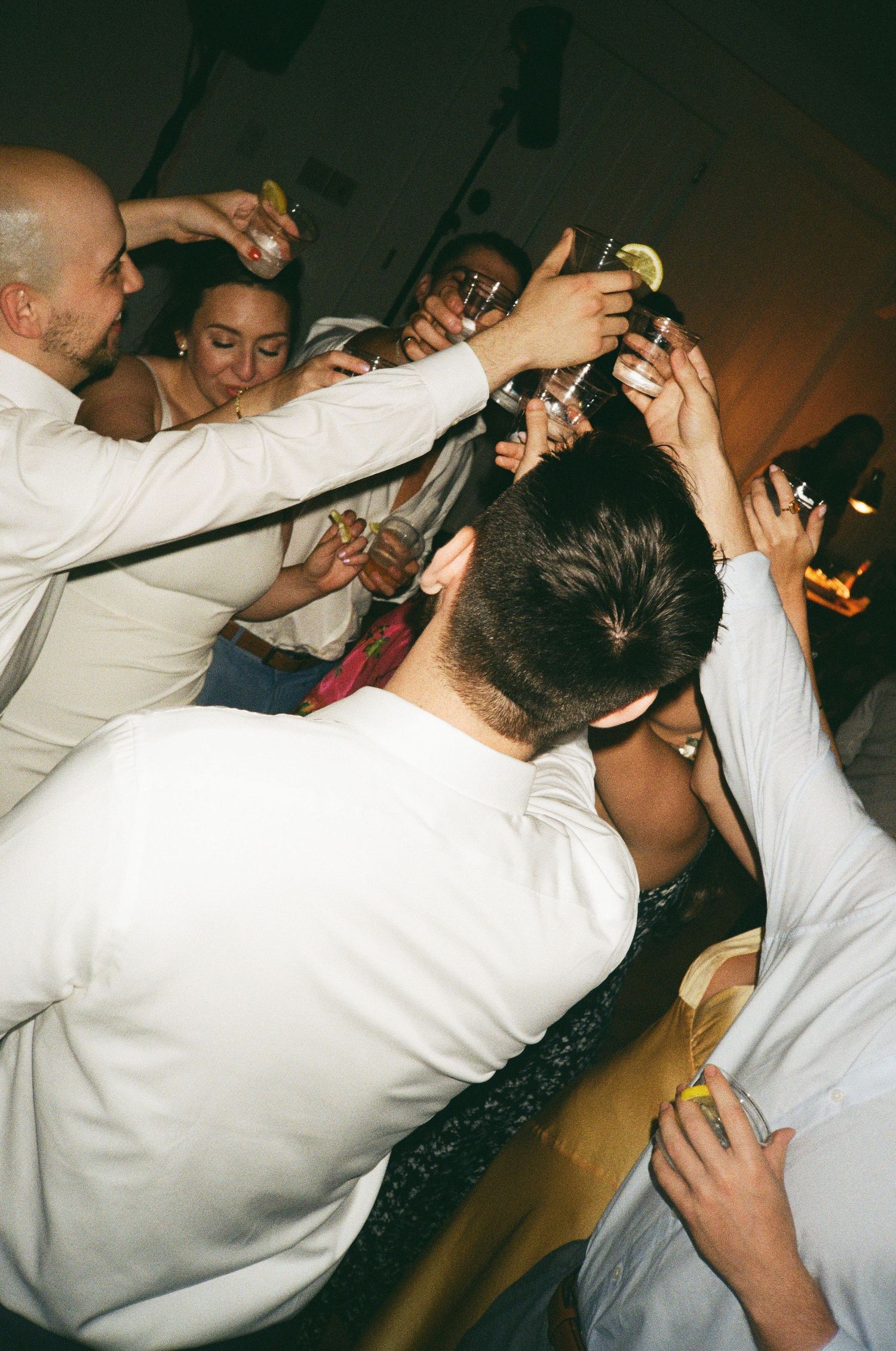 Group of people in white shirts dancing and raising drinks at a lively party celebration.