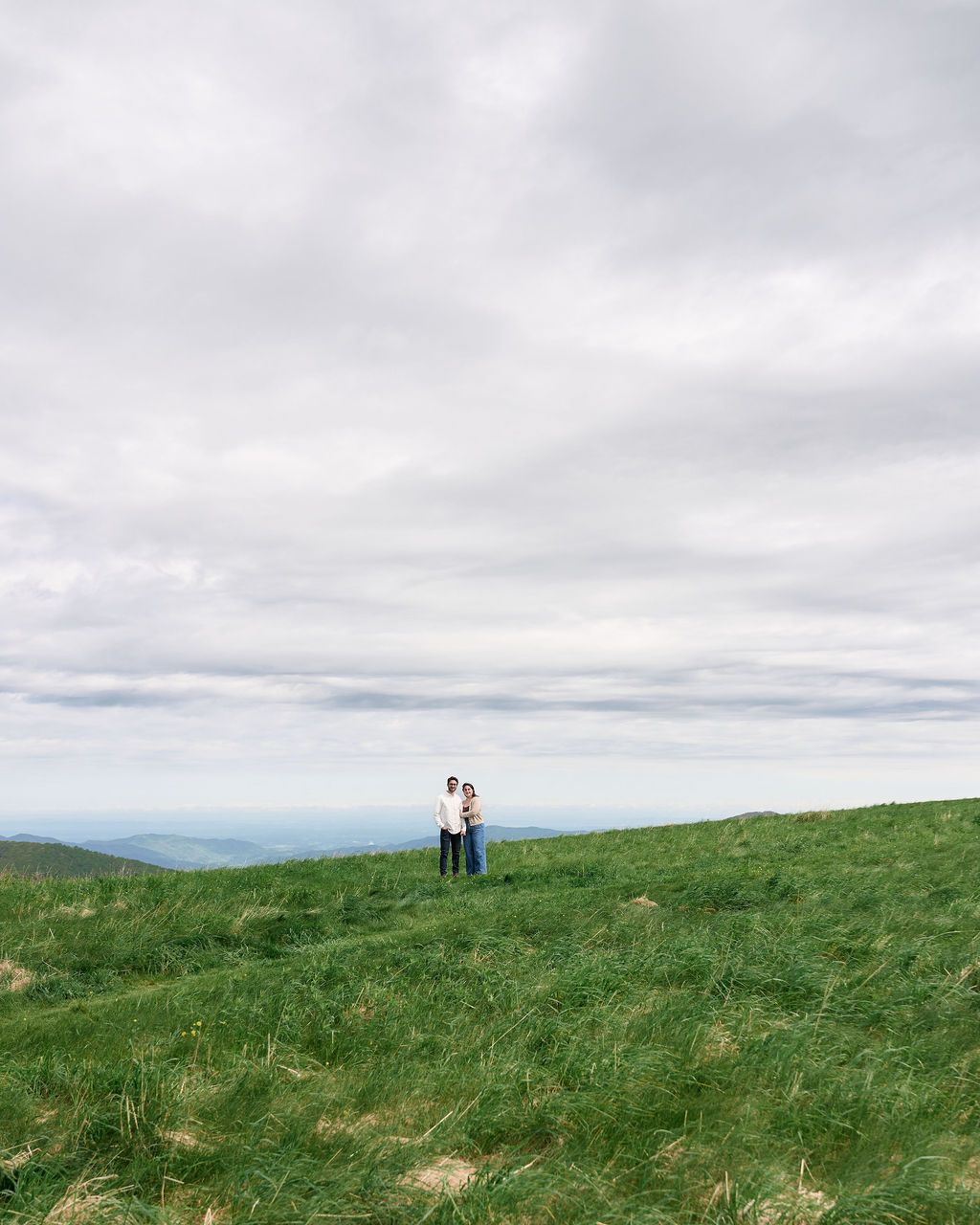 Two distant figures stand together on a rolling green hilltop beneath an overcast sky.