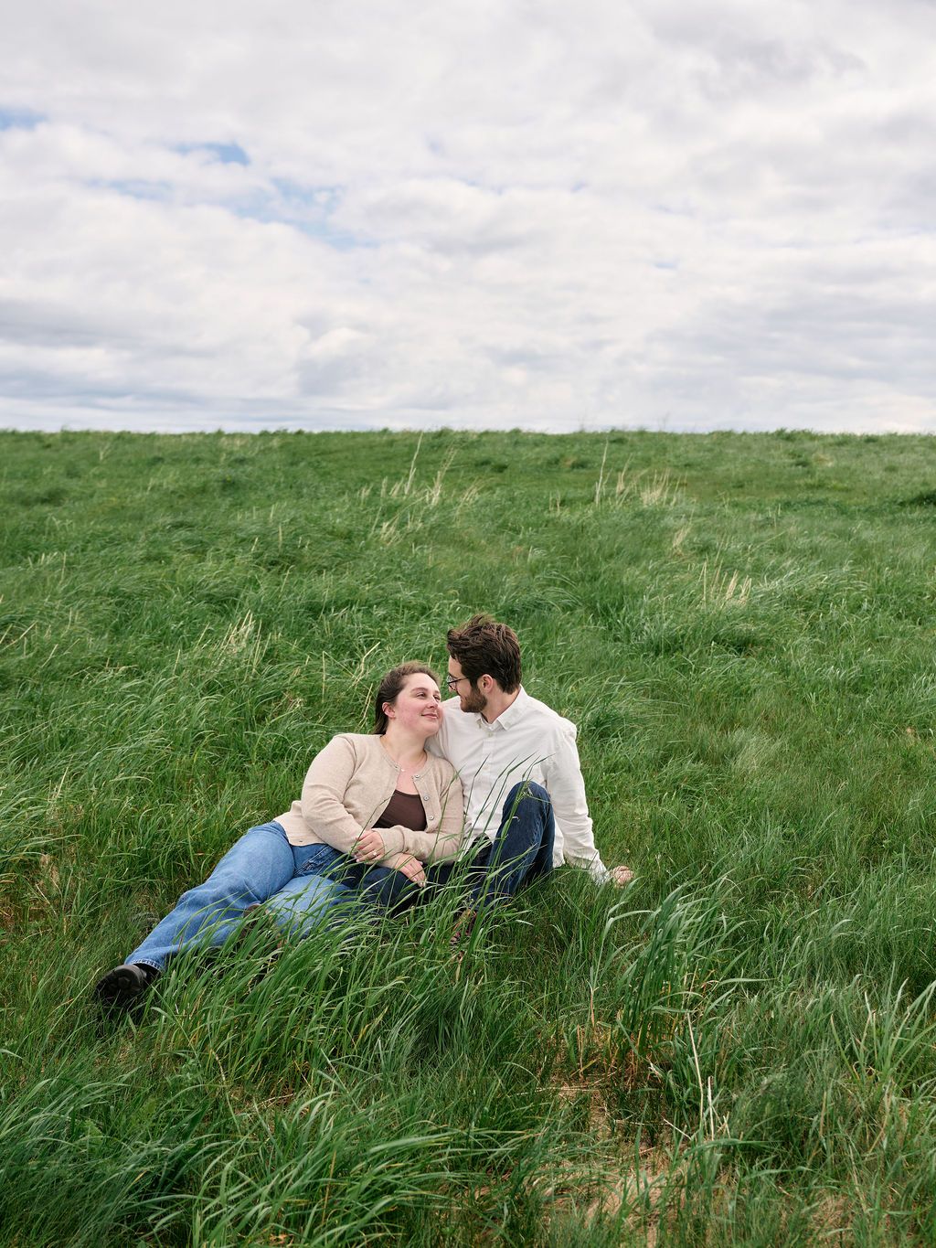 A romantic scene of a couple resting together in a lush green meadow under cloudy skies.