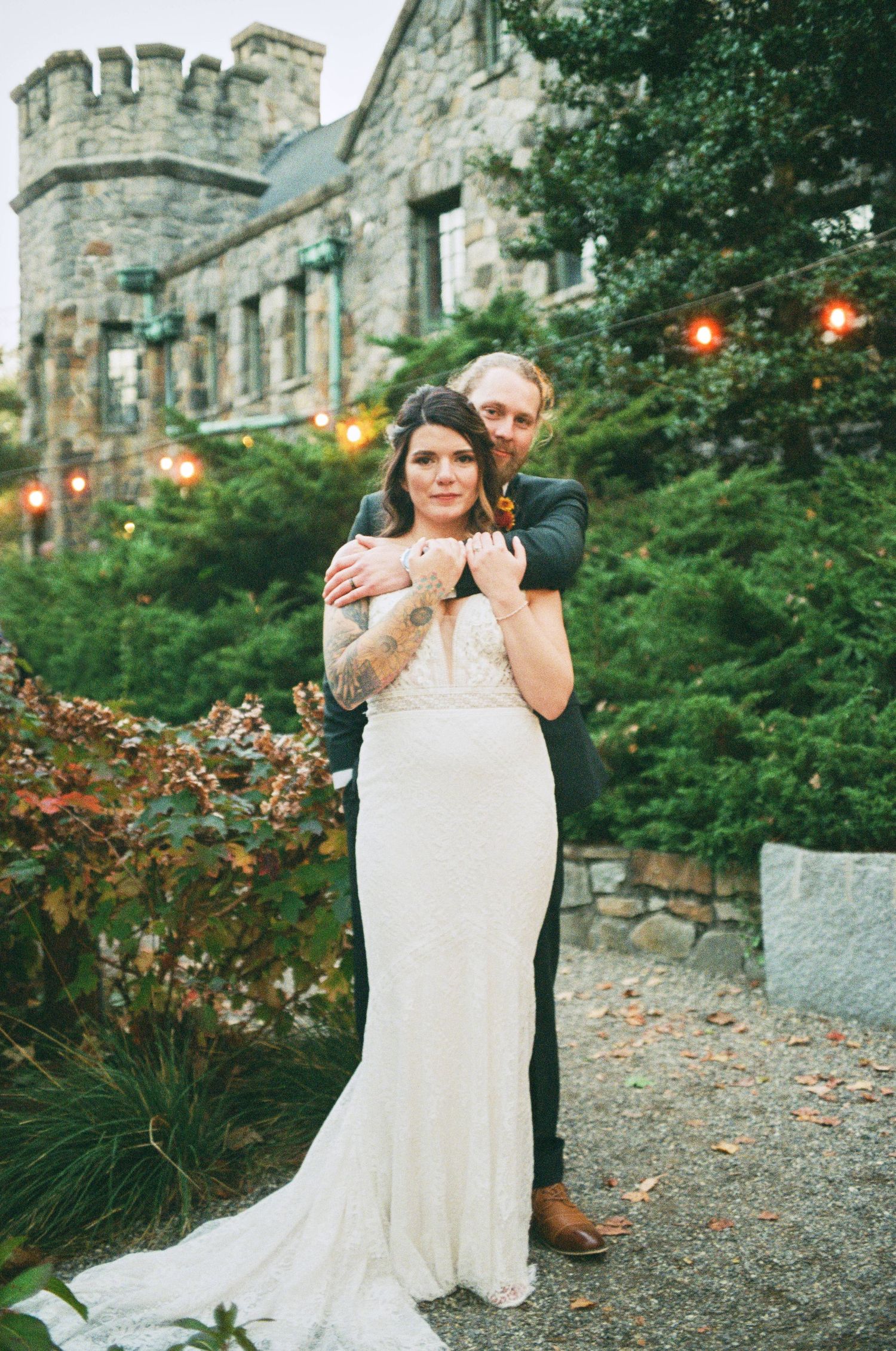 A romantic wedding portrait at a castle with string lights and greenery in the background.
