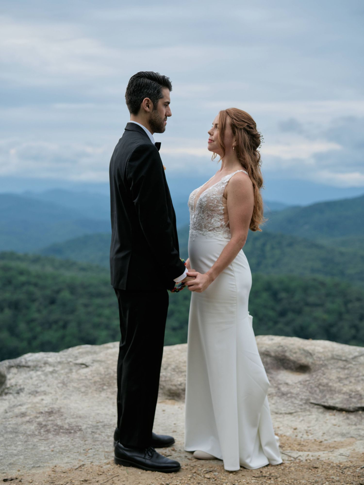 A couple shares an intimate moment during their mountaintop wedding ceremony against a backdrop of rolling hills and blue skies.