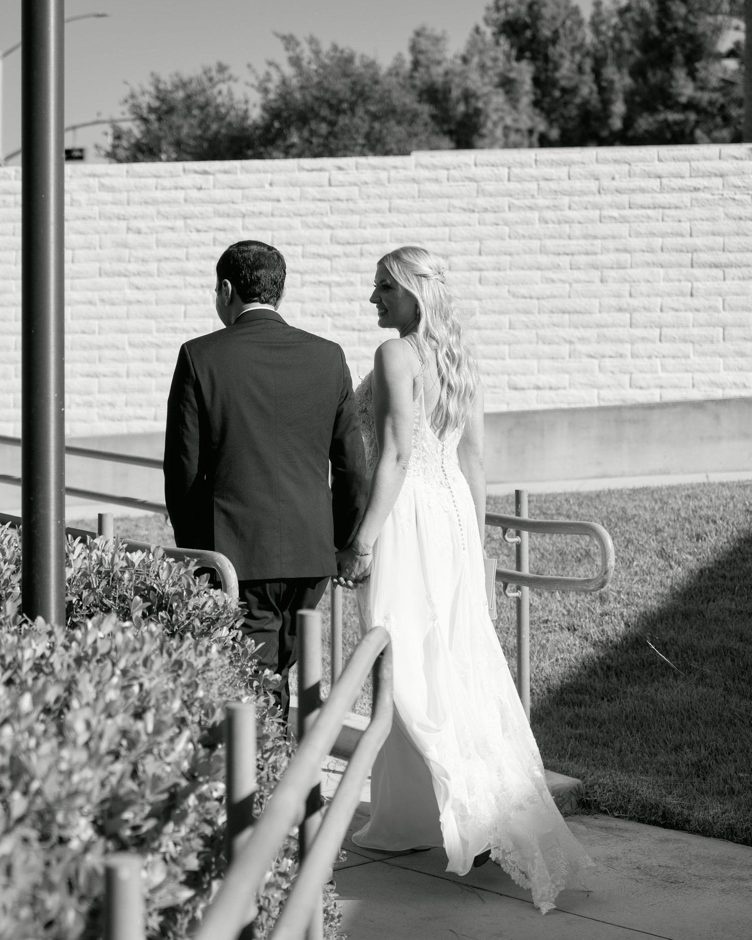Black and white photo of a couple walking together along a brick wall pathway.