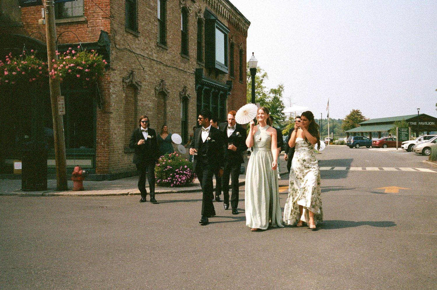 Group in formal attire standing on a street corner near a brick building in an urban setting.