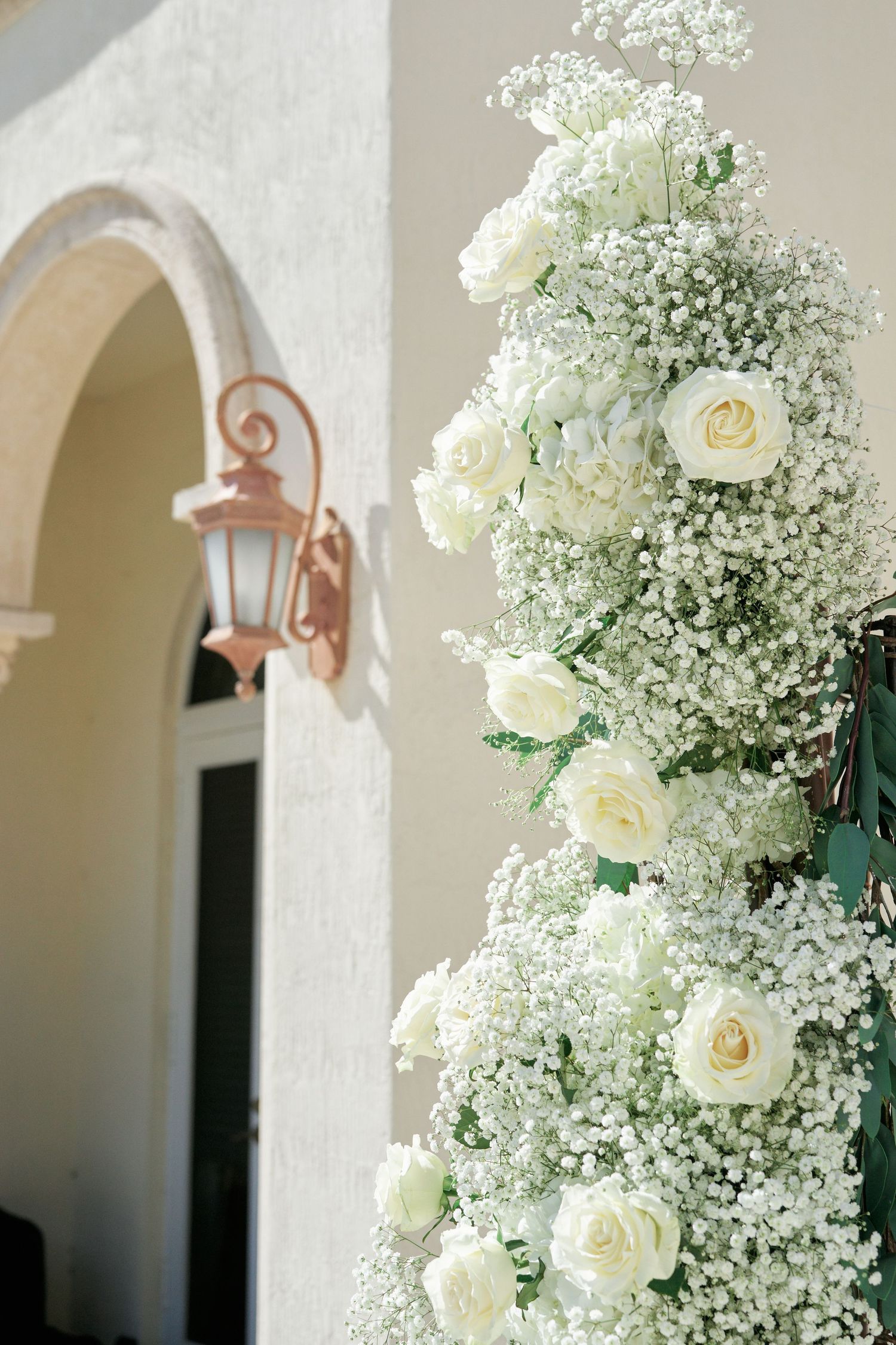 White roses and baby's breath floral arrangement adorning an archway entrance at an elegant venue.
