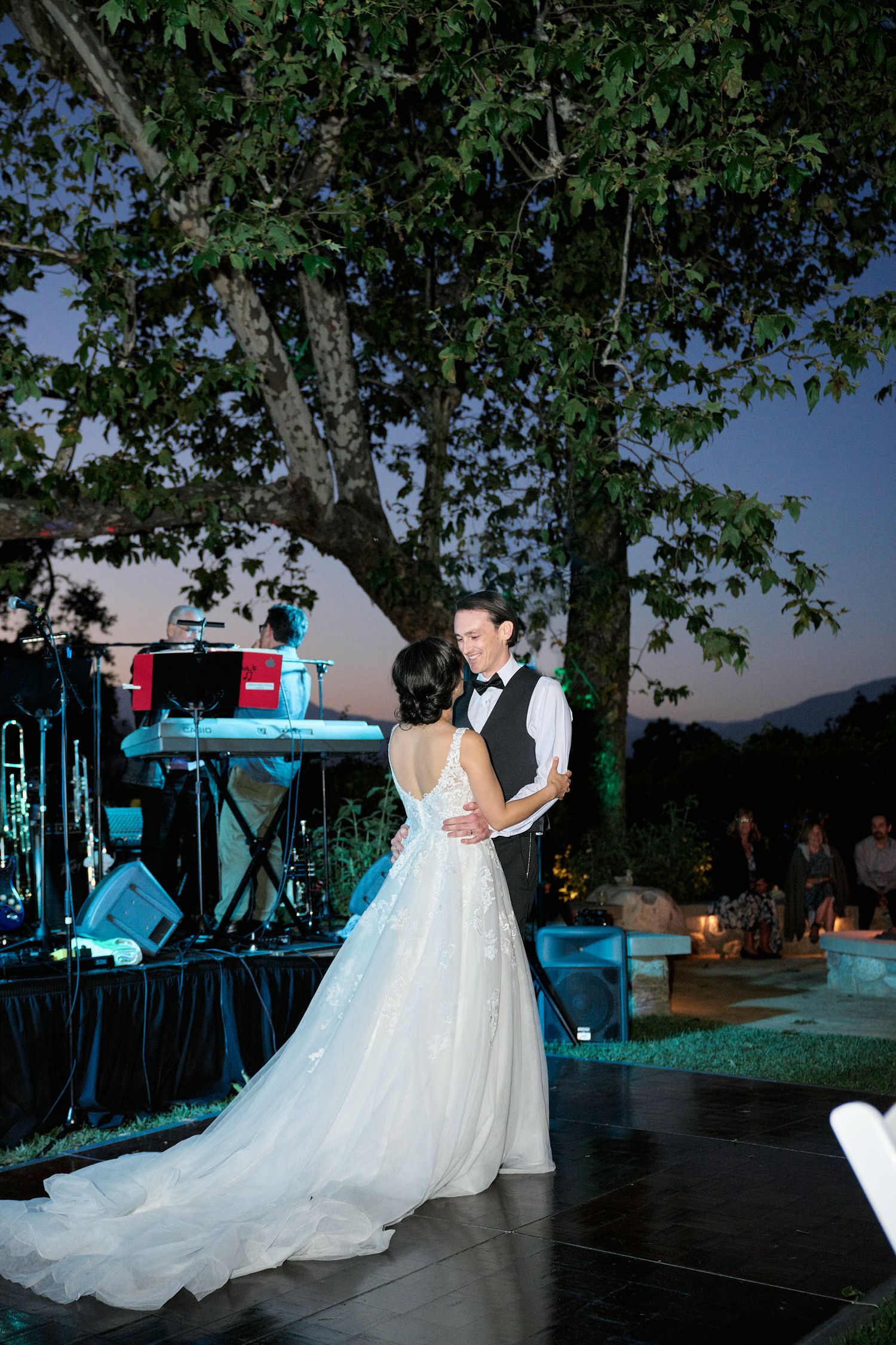 Evening wedding dance on outdoor patio with band setup and blue lighting.