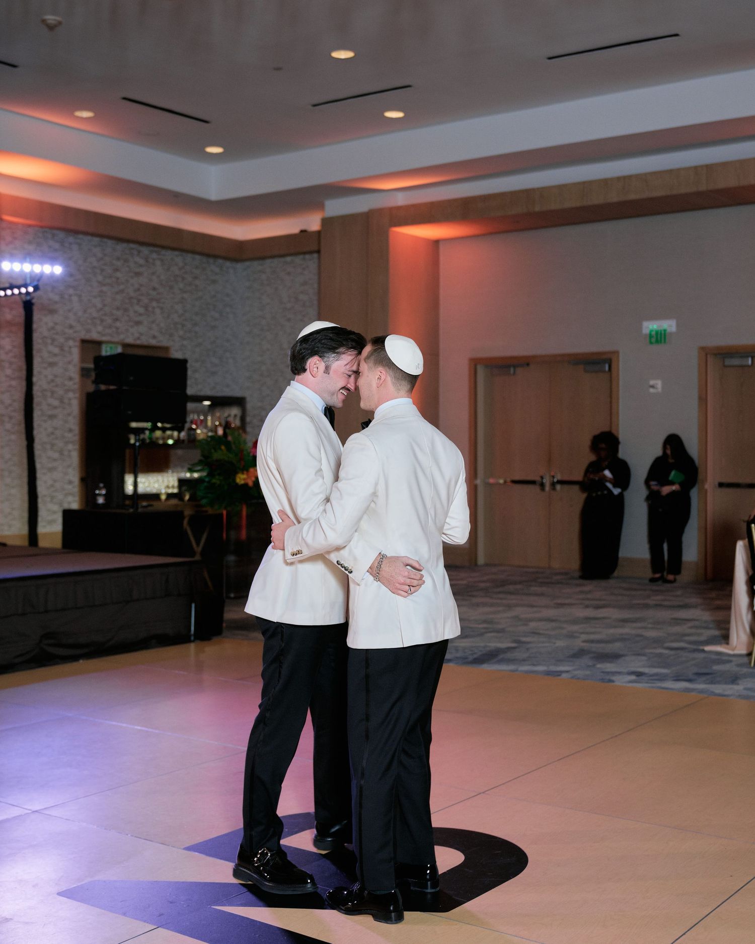 Two chefs in white coats share a romantic dance moment on the ballroom floor under warm ambient lighting.