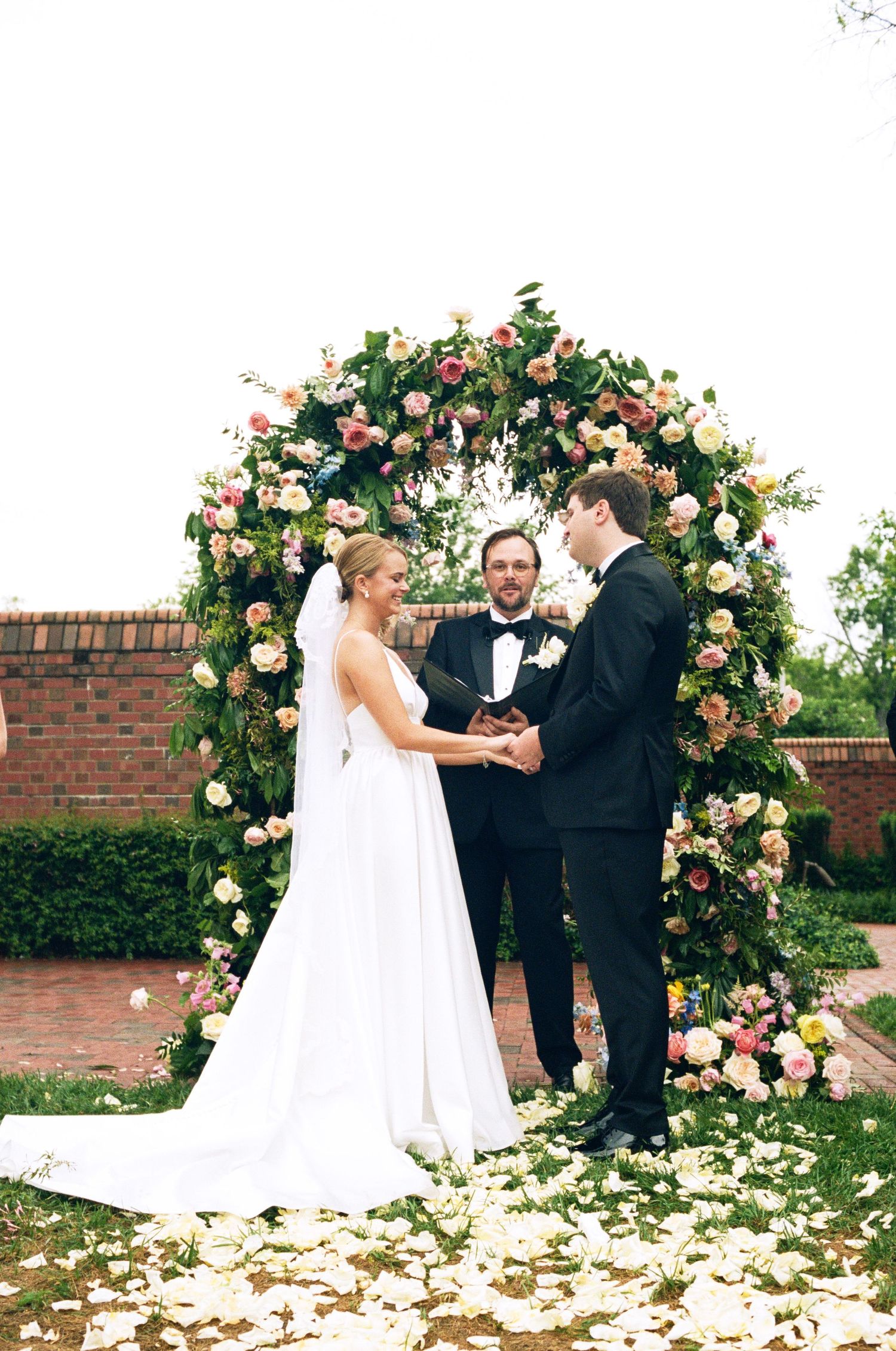 Wedding ceremony under a beautiful floral arch with peach and pink roses.