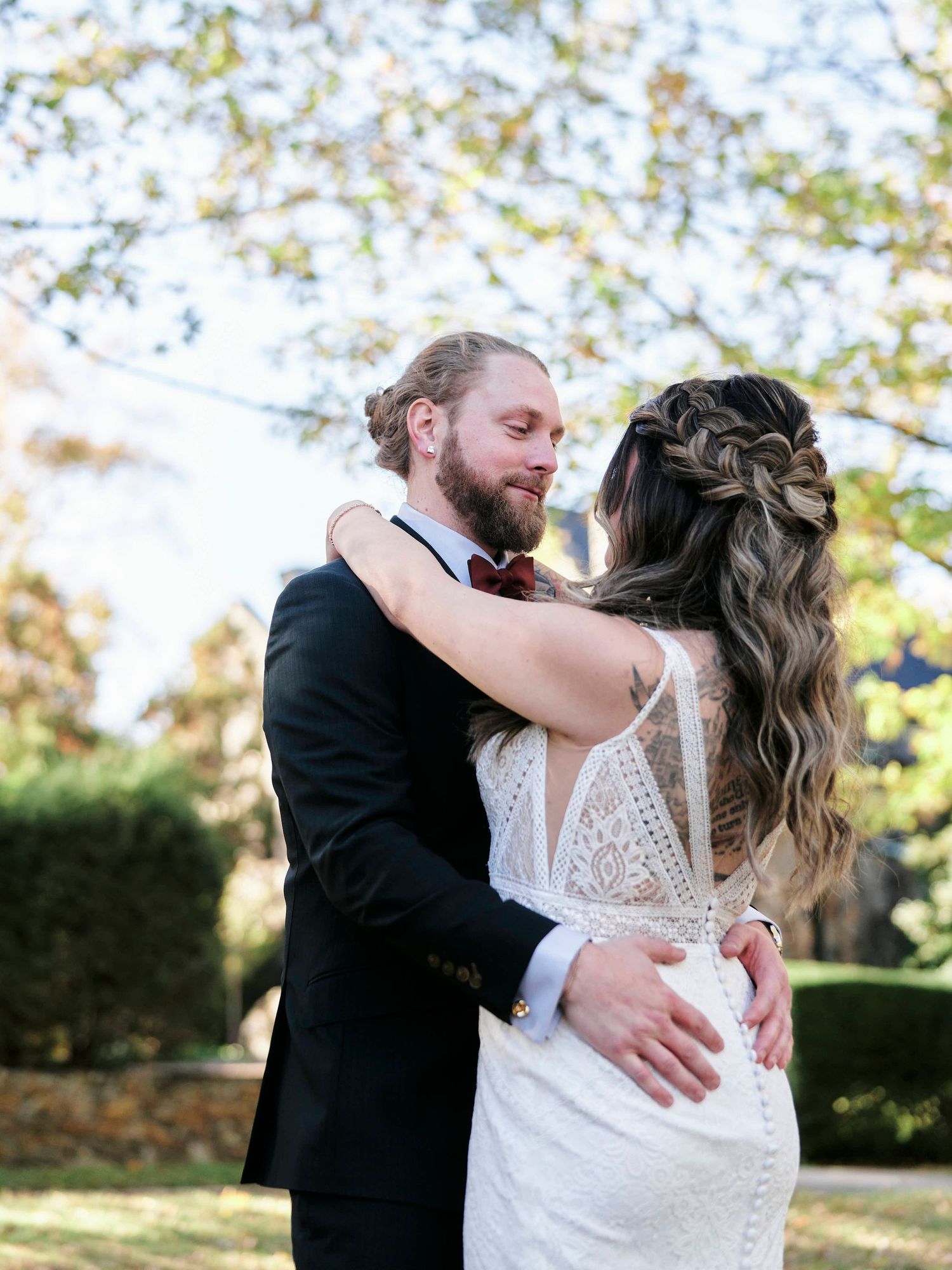 Newlywed couple embracing outdoors in sunlit garden setting.