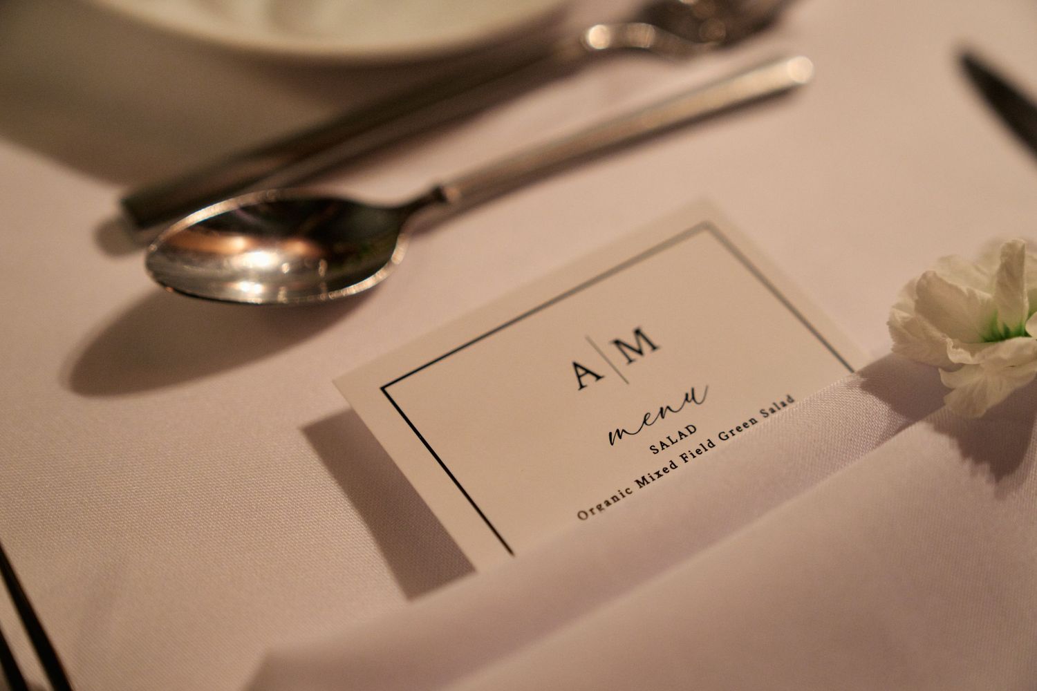 Wedding menu card with AM monogram placed on elegant table setting.