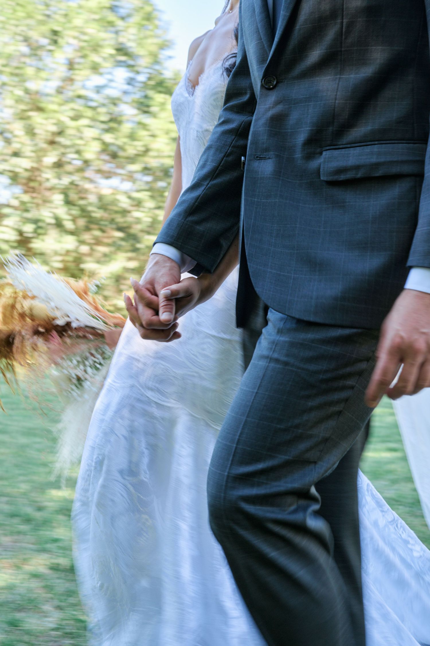 A close-up shot of a couple holding hands during their wedding ceremony, showing dress and suit details.