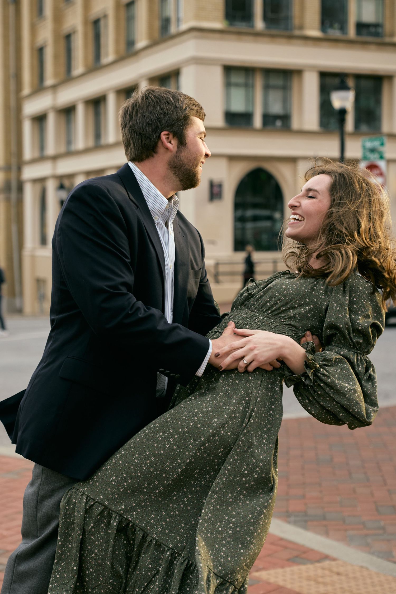 A couple laughs together during a dance pose on a brick sidewalk downtown.