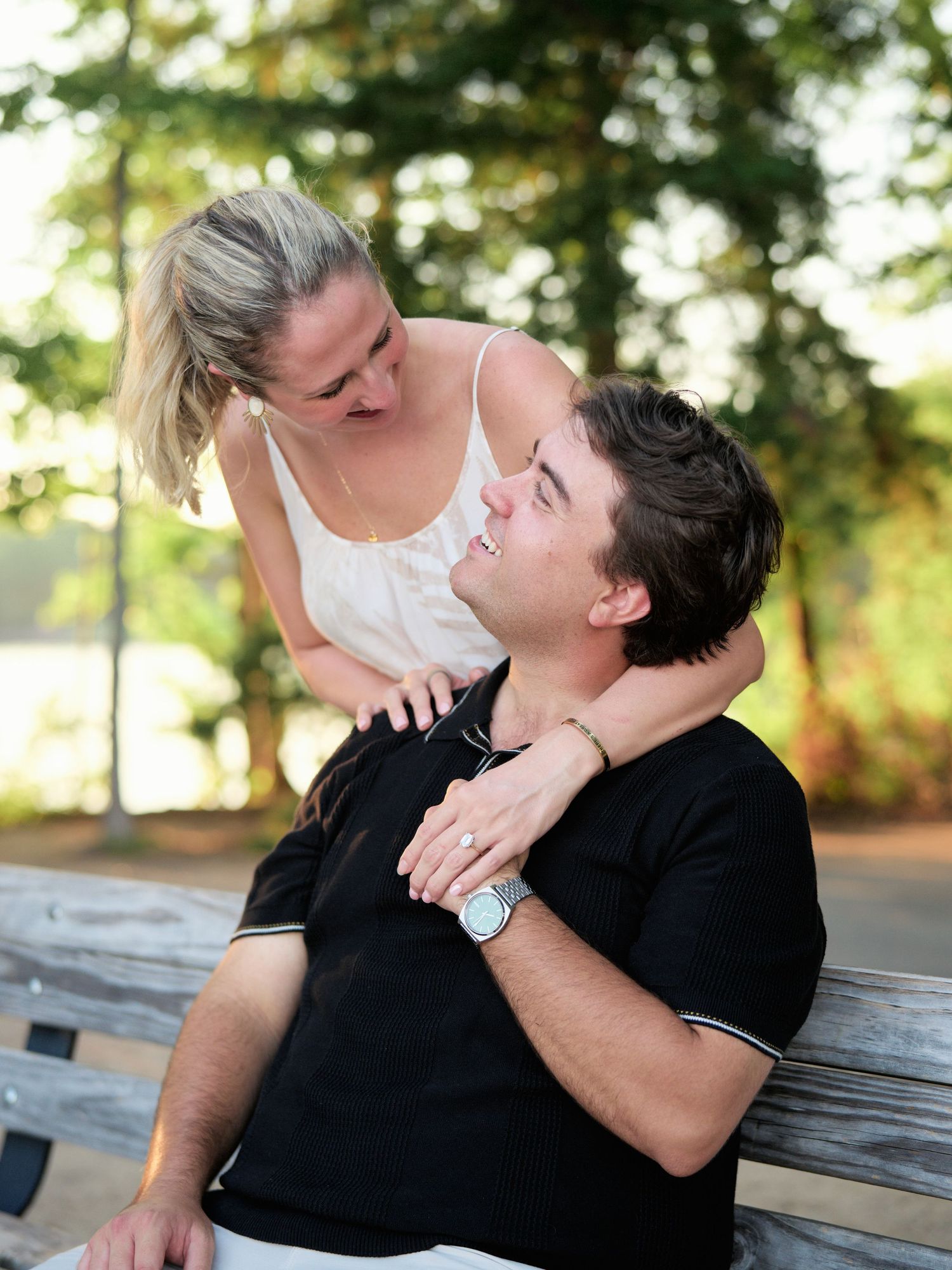 A couple shares an intimate moment together while sitting outdoors on a wooden bench in a natural setting.