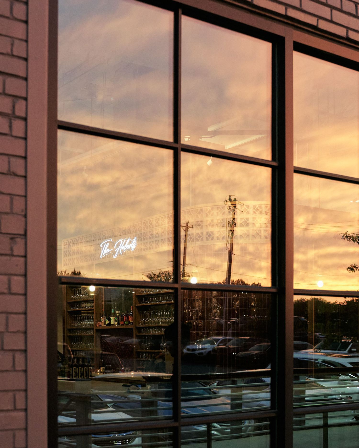 Sunset reflected in large windows of The Hobby restaurant with neon sign visible.