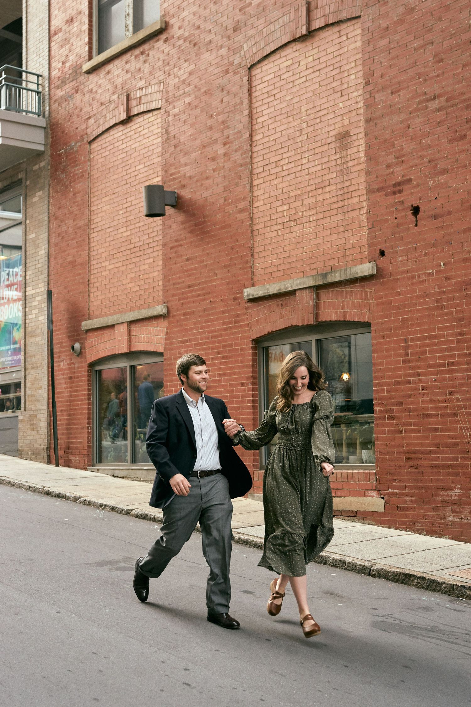 A couple dances playfully on a brick-lined street in front of an industrial building.