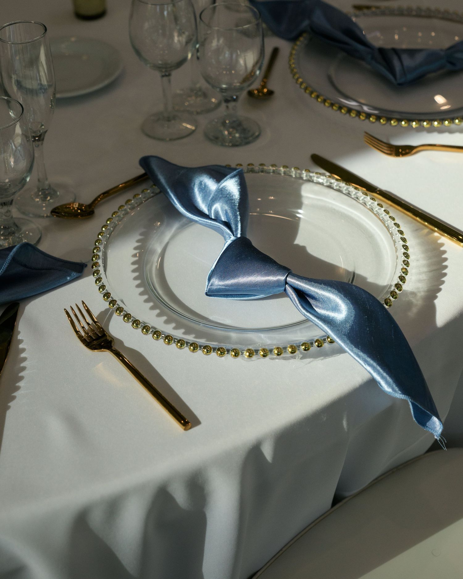 An elegant place setting features a dusty blue napkin and gold-rimmed plate at a formal dinner table.