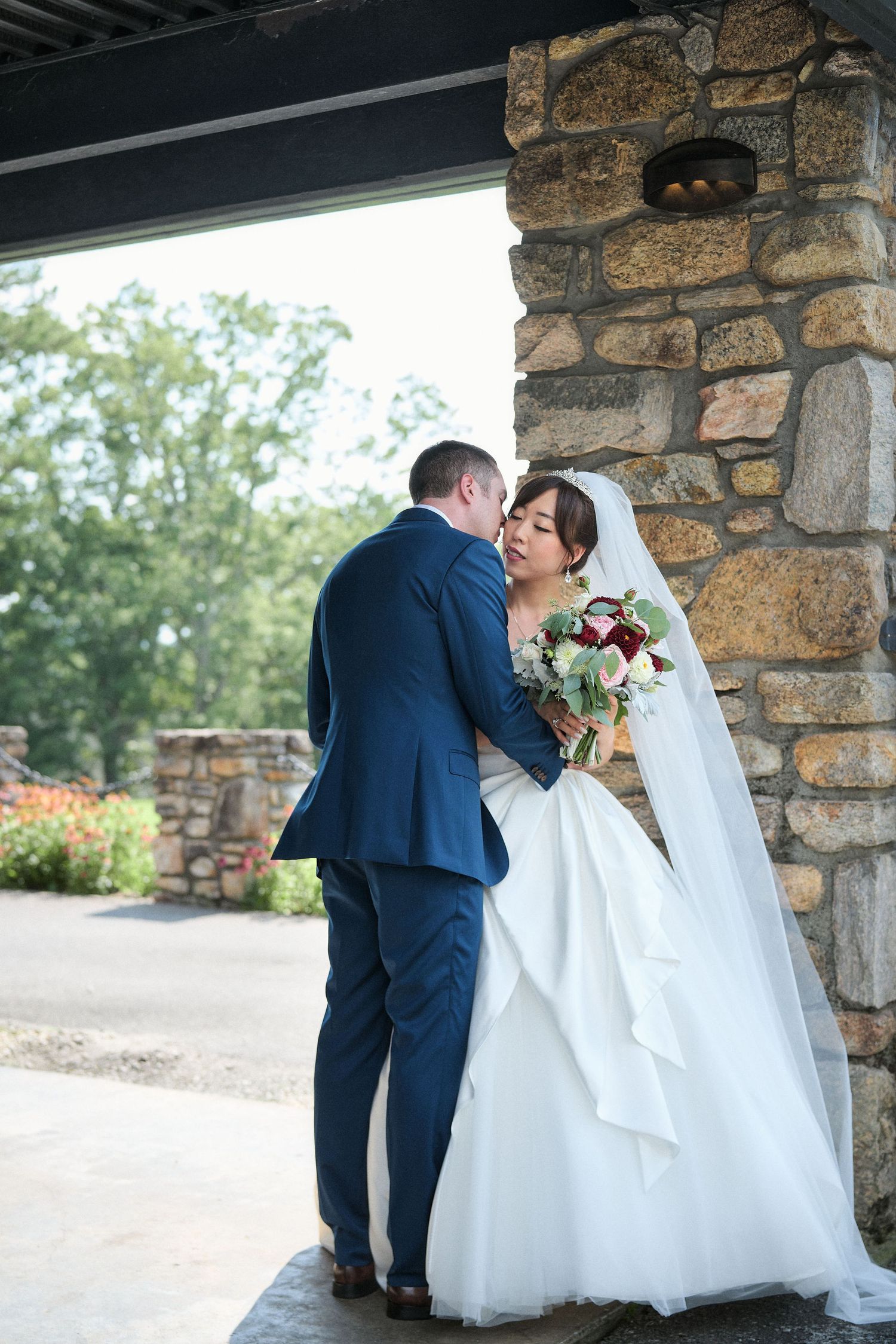 A romantic moment between newlyweds beneath a stone archway with floral bouquet.