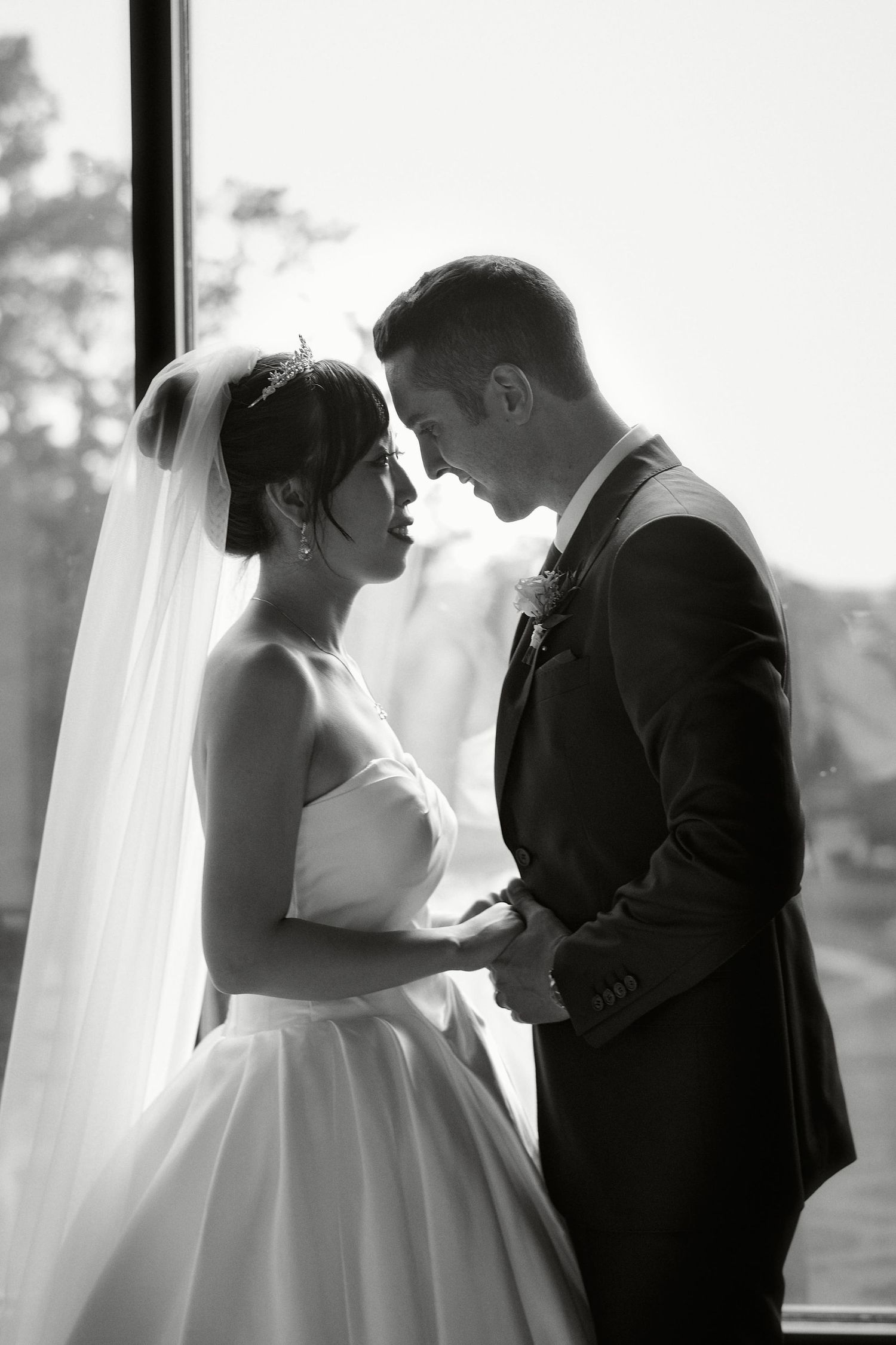 Black and white portrait of newlyweds in an intimate pose by a bright window.