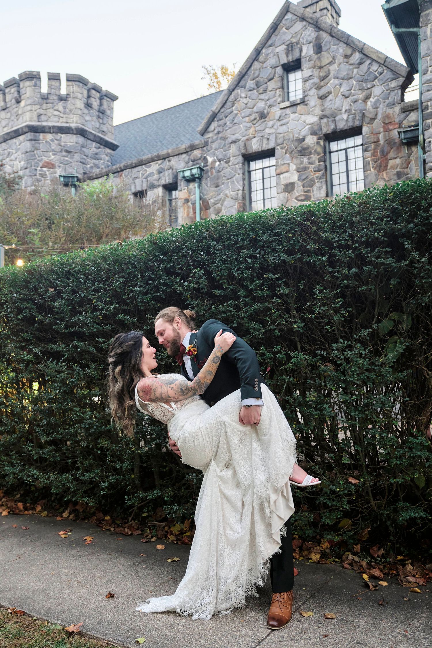 A romantic wedding moment captured in front of a historic stone castle with hedges.