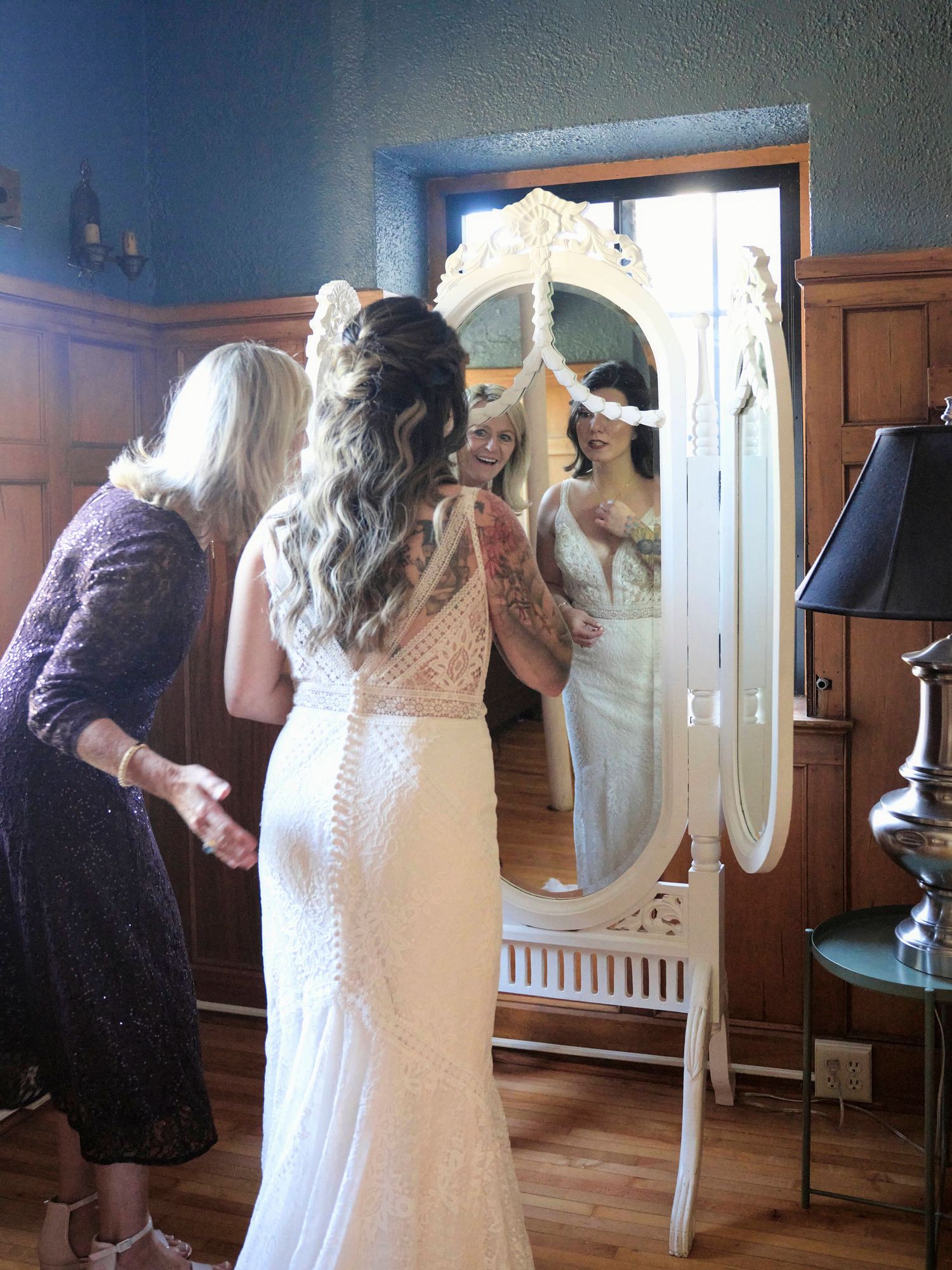 People gathered around an ornate white mirror during wedding preparations.
