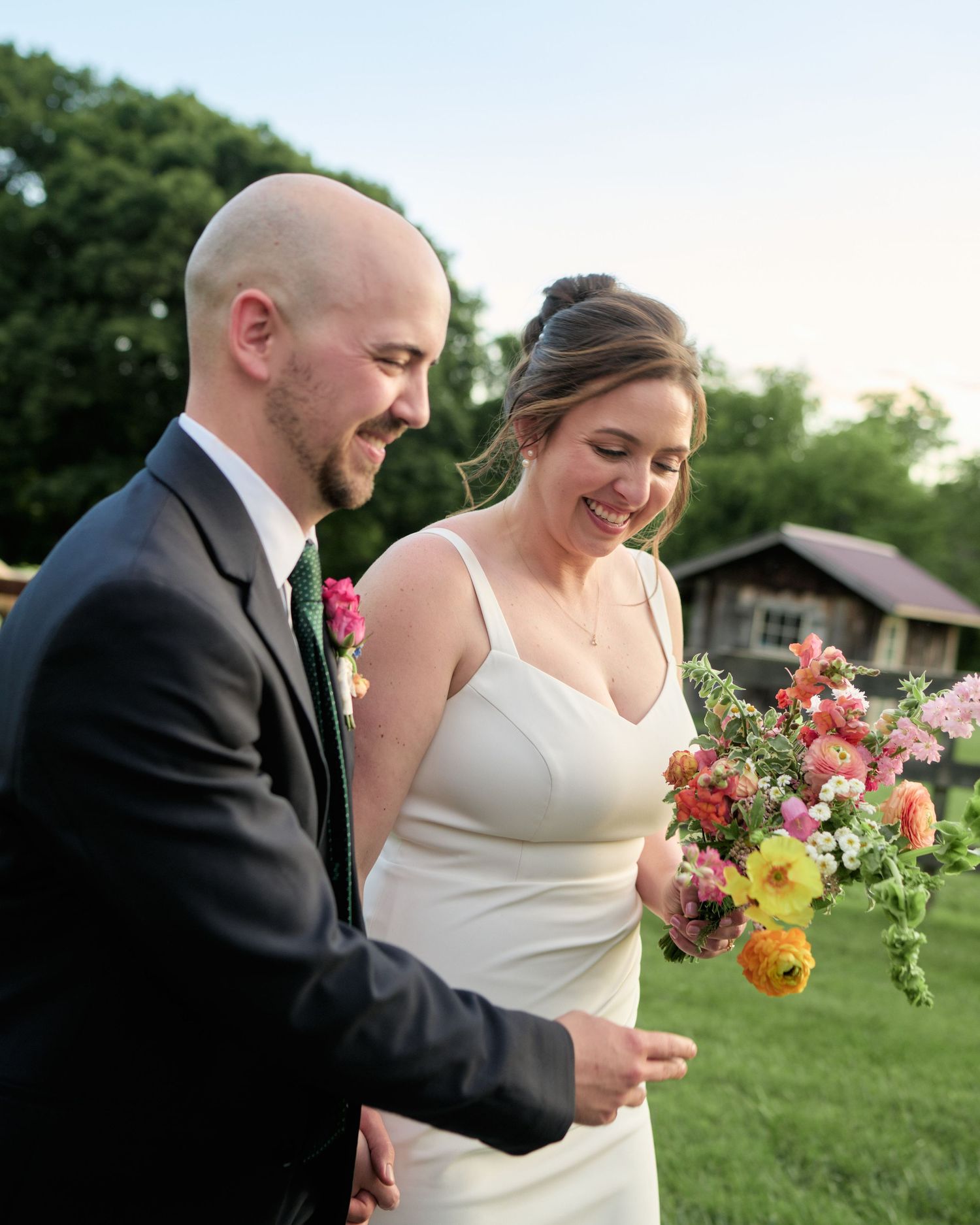 Happy couple shares a laugh while holding colorful bouquet on venue grounds.